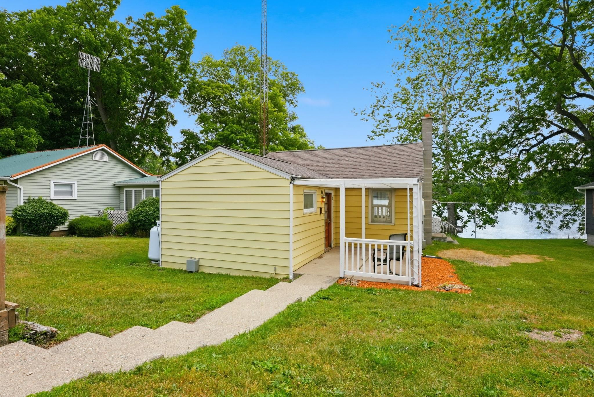 Yellow siding home featuring a covered front porch with white railings, a concrete walkway, and a chimney structure