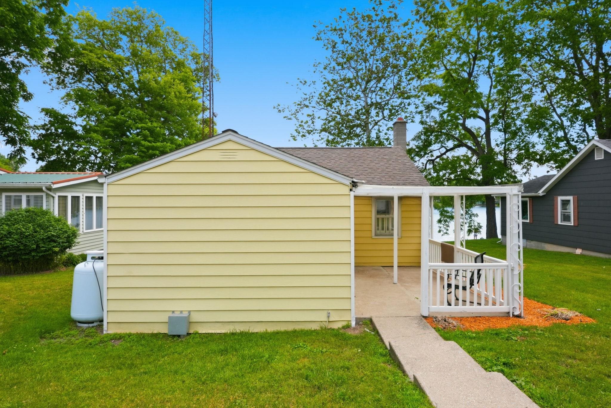 Yellow siding exterior featuring a covered patio, concrete walkway, and shingle roof