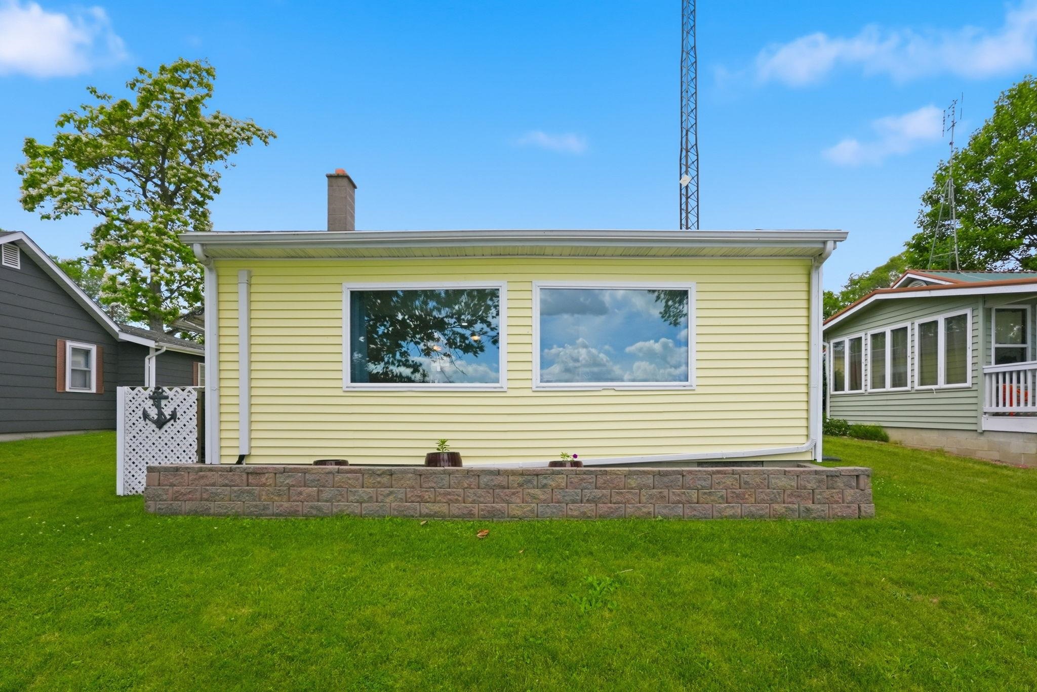 Yellow siding exterior with two large windows and a stone retaining wall