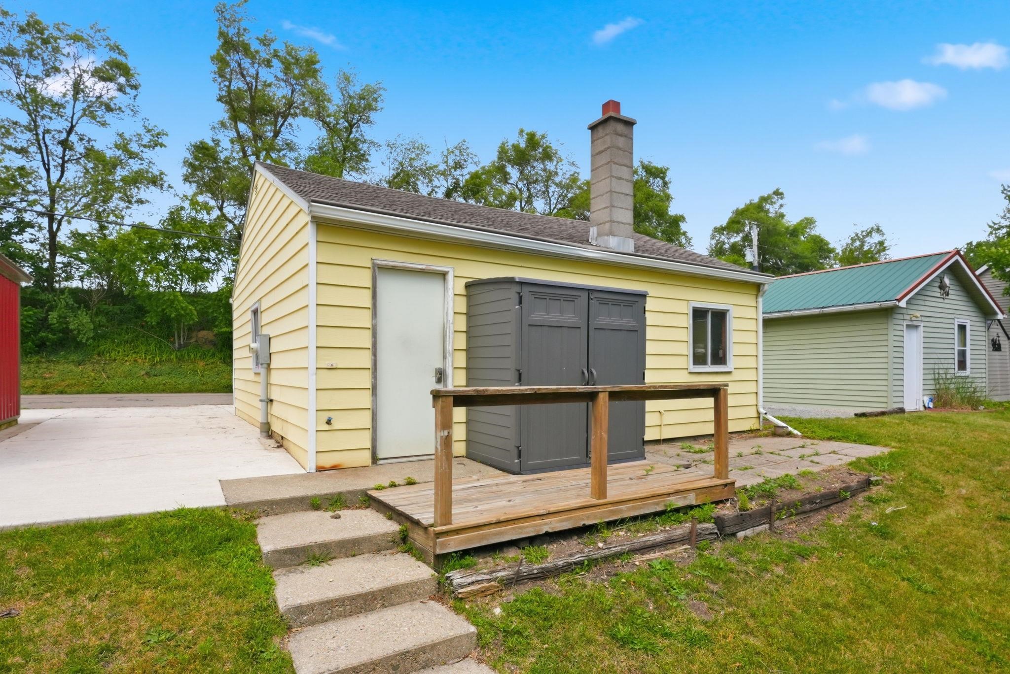 Yellow siding structure featuring a concrete chimney, a rear concrete patio, and a concrete pathway