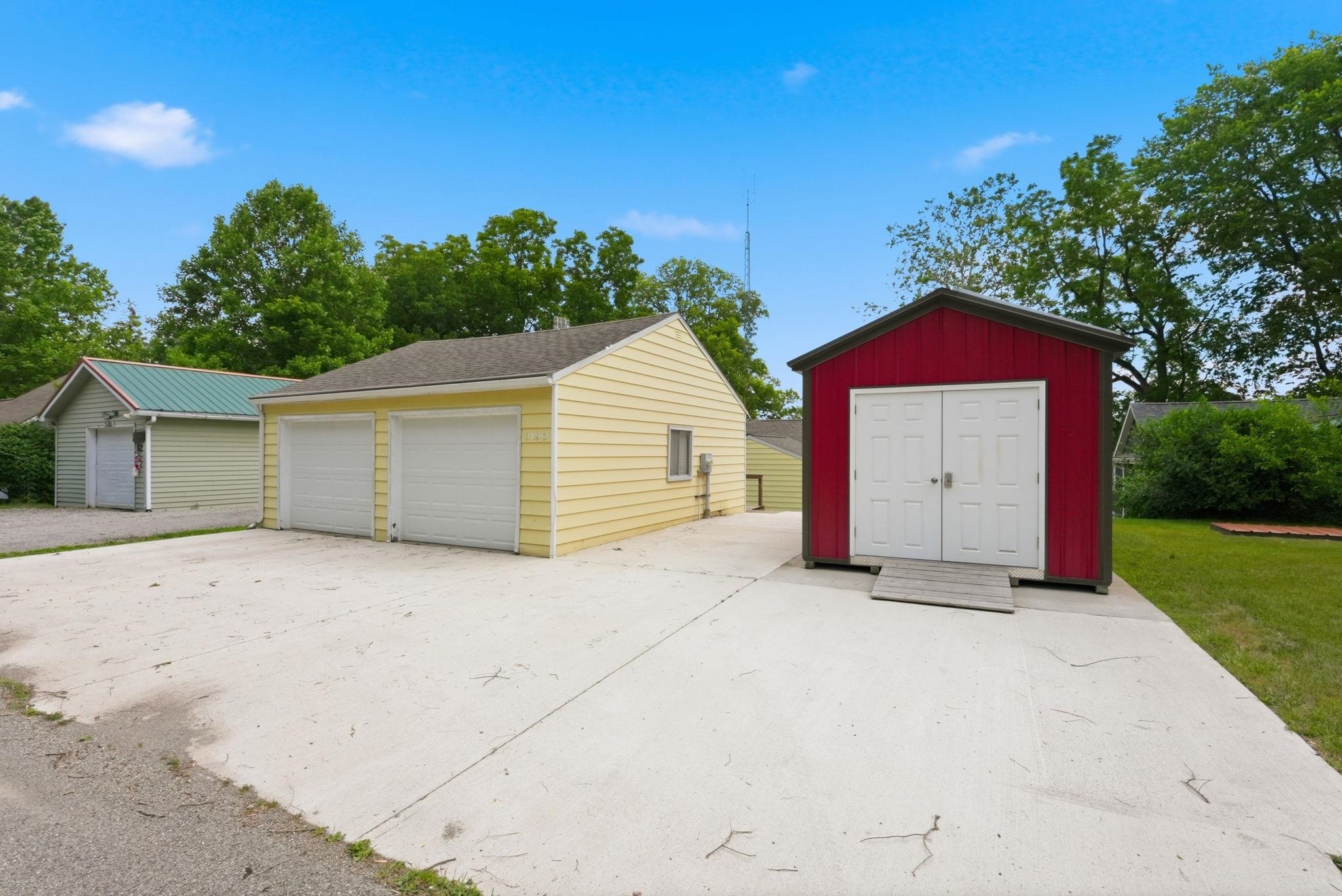 Two-car detached garage with white overhead doors, accompanied by a red storage shed with white double doors
