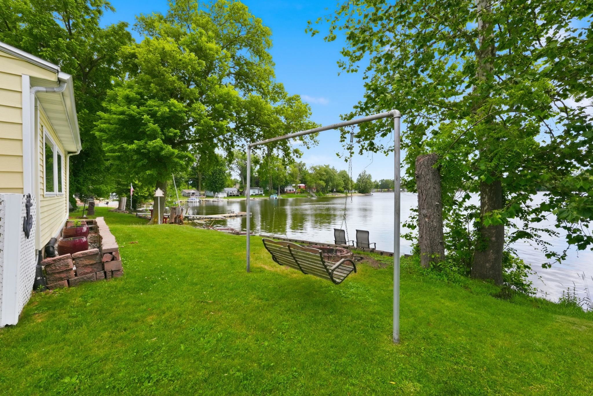 Expansive waterfront lawn featuring mature trees and a metal swing set