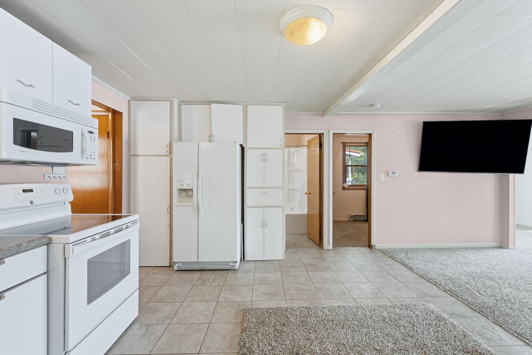 Kitchen area featuring white cabinetry, white appliances, and light gray tiled flooring