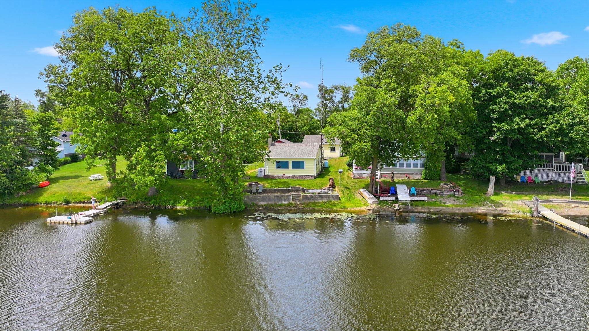 Waterfront property featuring multiple docks, mature trees, and a grassy shoreline