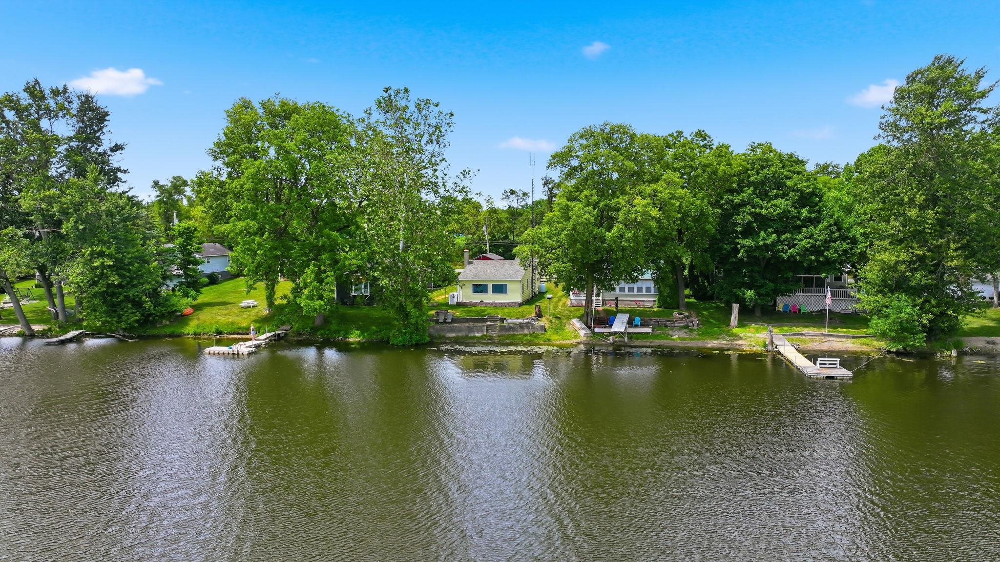 Waterfront property featuring multiple docks, mature trees, and a clear blue sky