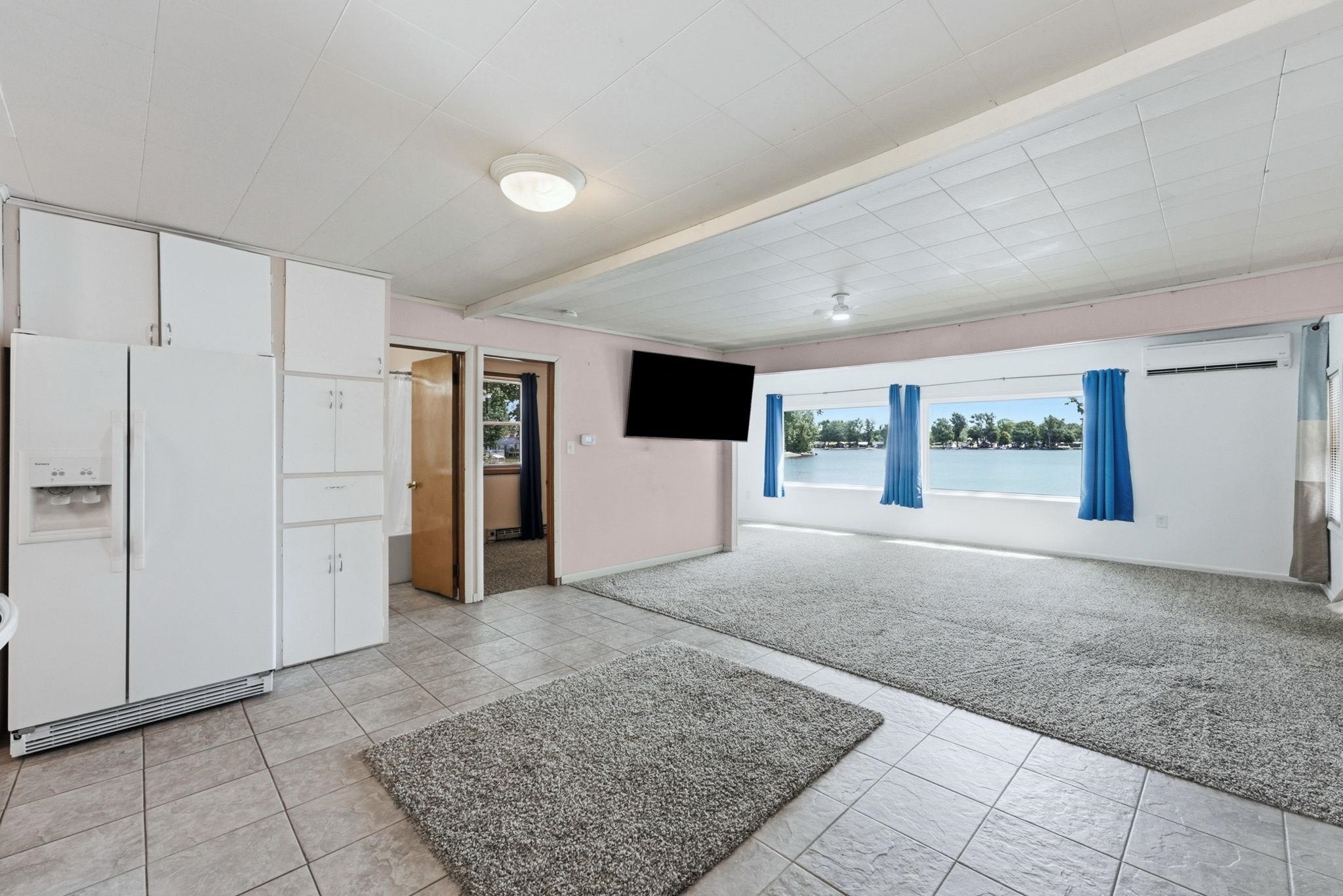 Expansive room featuring multiple windows with water scenery, tile flooring, wall-mounted air conditioning unit, and built-in white cabinetry