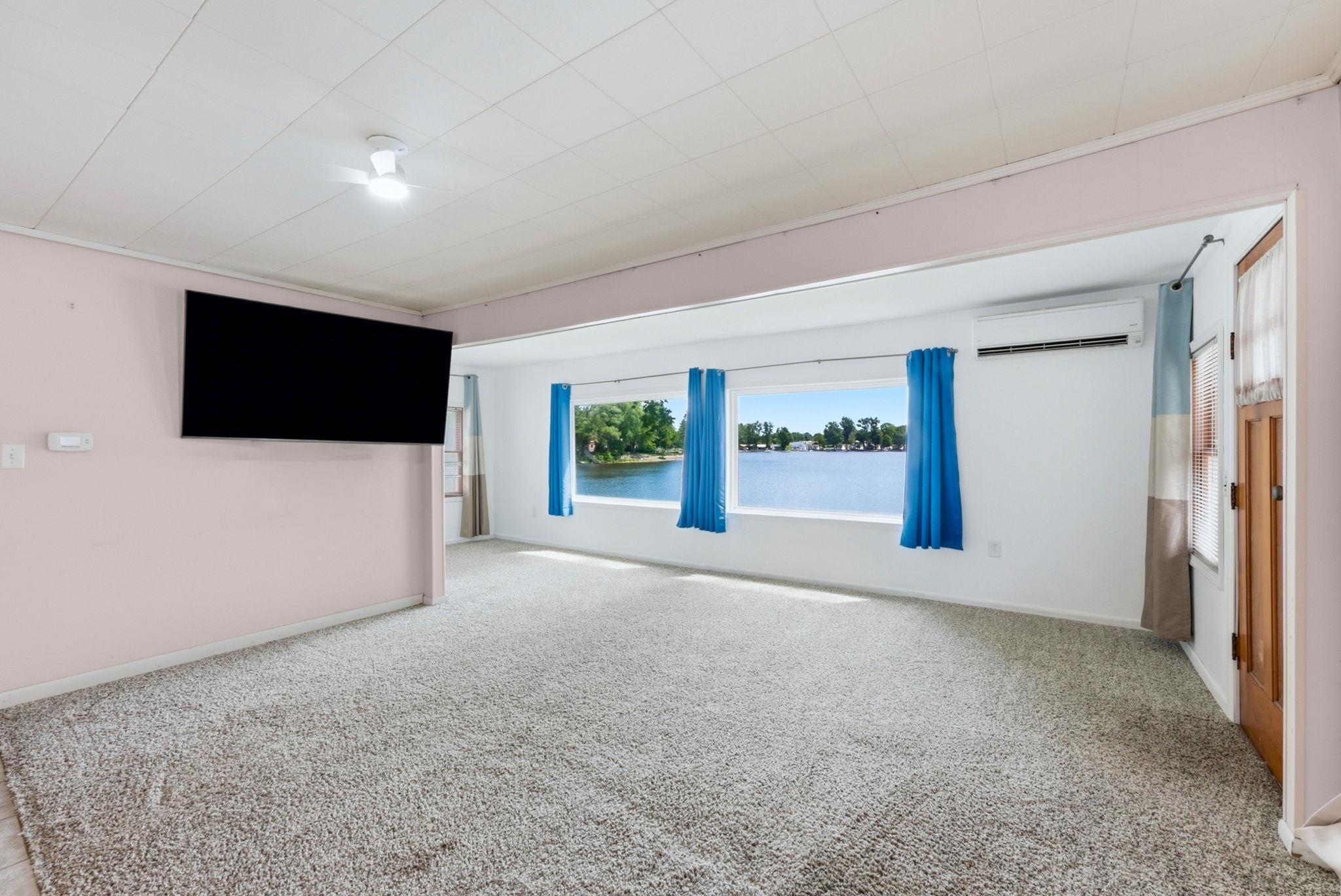 Carpeted living area featuring a large picture window, water scenery, light-toned walls, and a mounted air conditioning unit