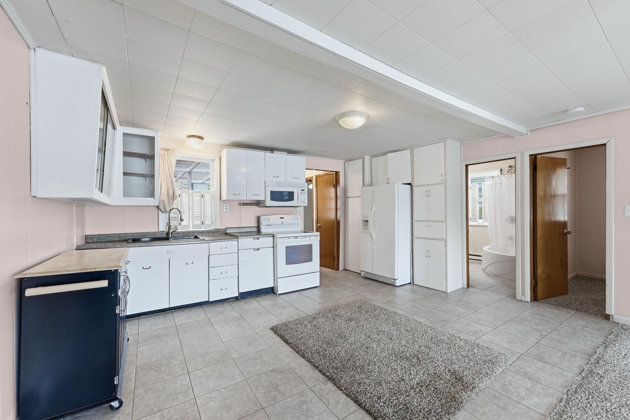 Kitchen featuring white cabinetry, gray countertop, tile flooring, and integrated white appliances