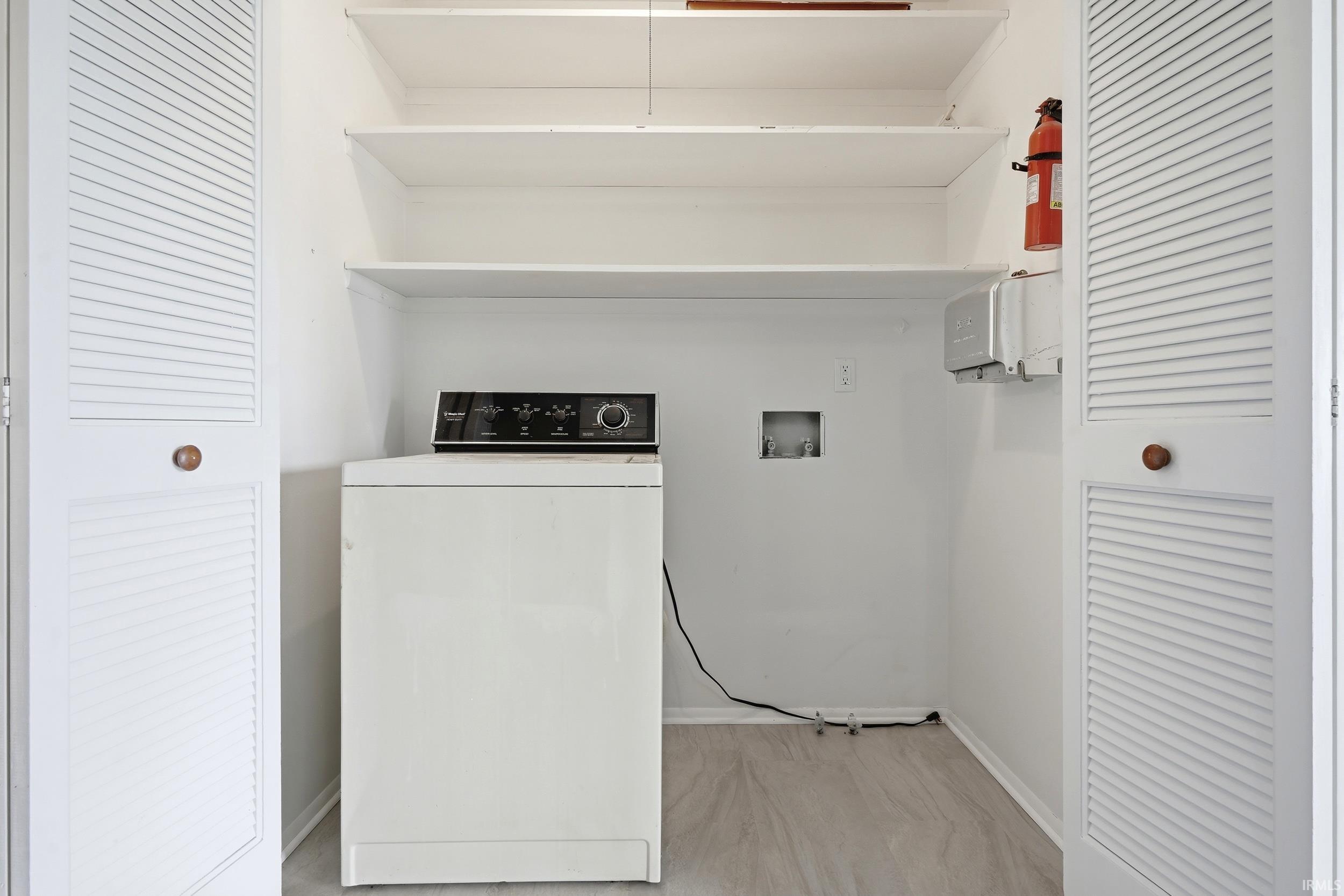 Dedicated laundry closet featuring a white washing machine, integrated shelving, and louvered bi-fold doors