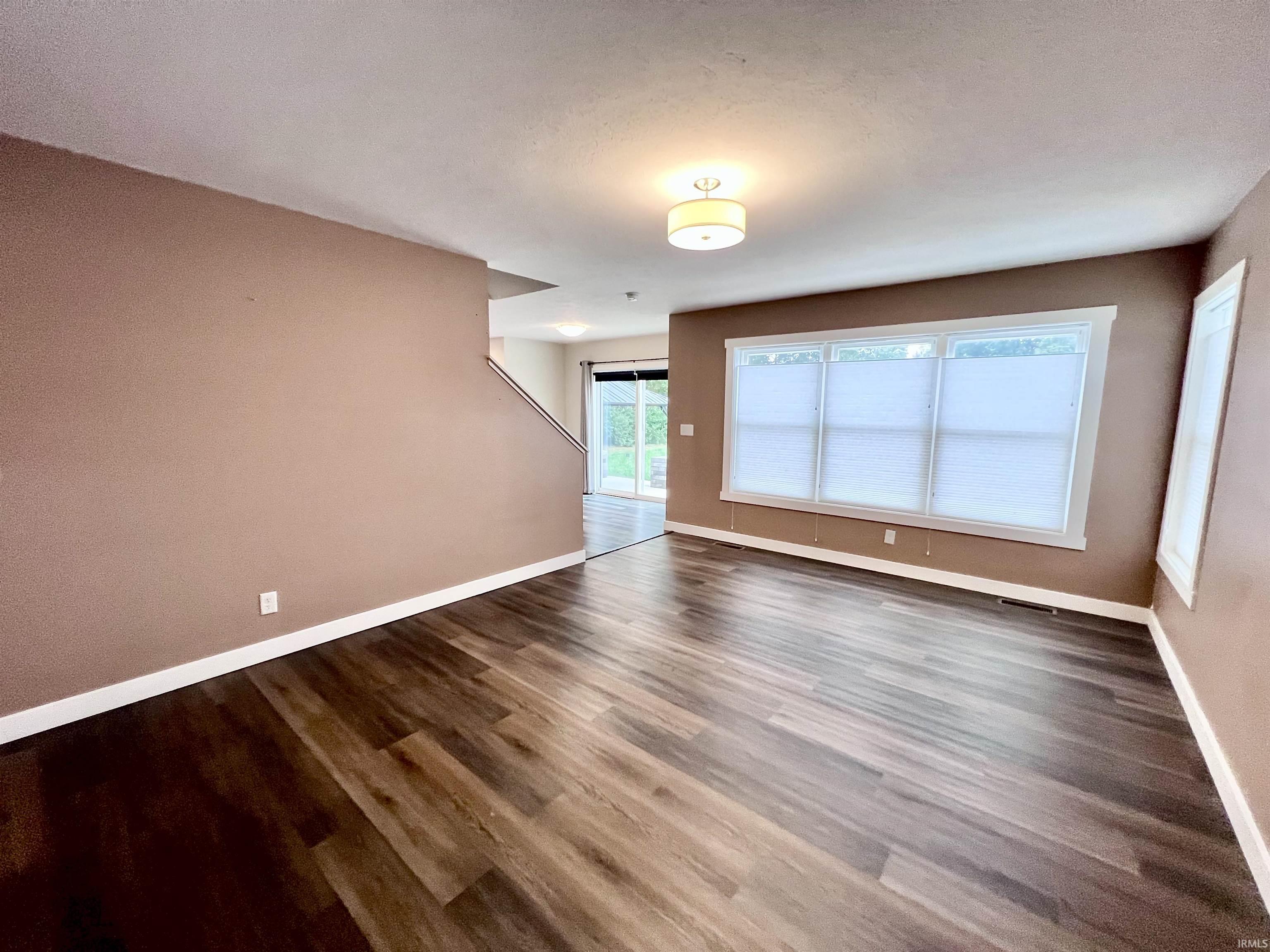 Spacious open living area showcasing wood-finish flooring, warm taupe walls, and abundant natural light from large multi-pane windows