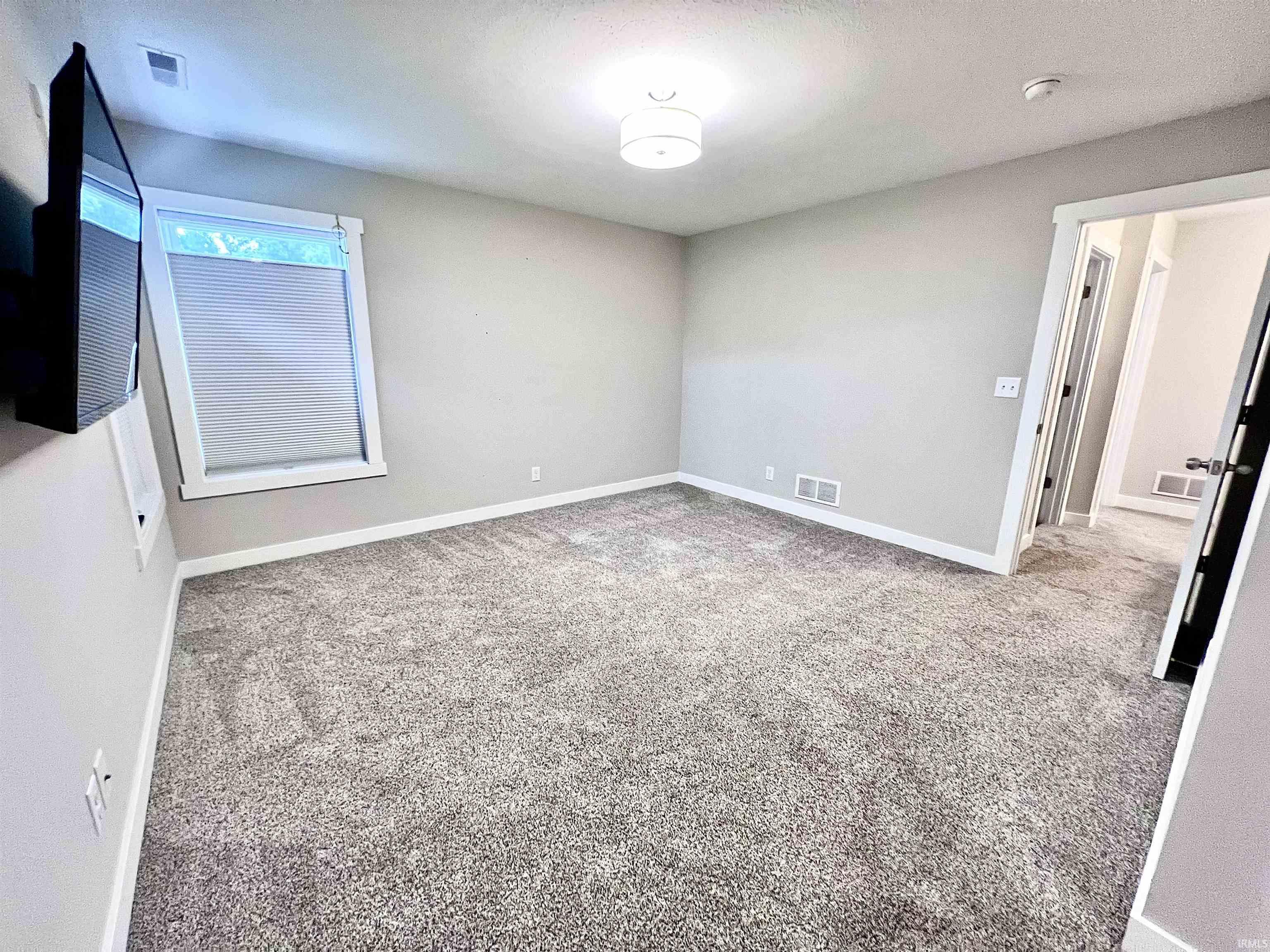 Spacious bedroom with neutral wall finishes, plush carpeting throughout, and abundant natural light from a large casement window