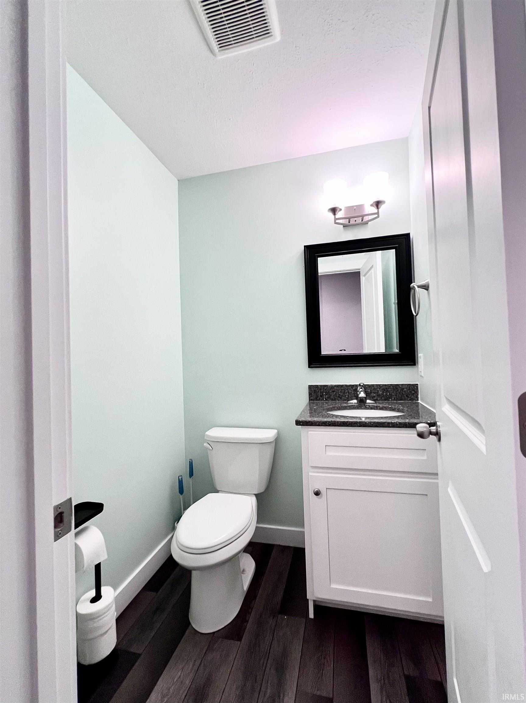 White vanity with dark countertop, undermount sink, and wall-mounted mirror