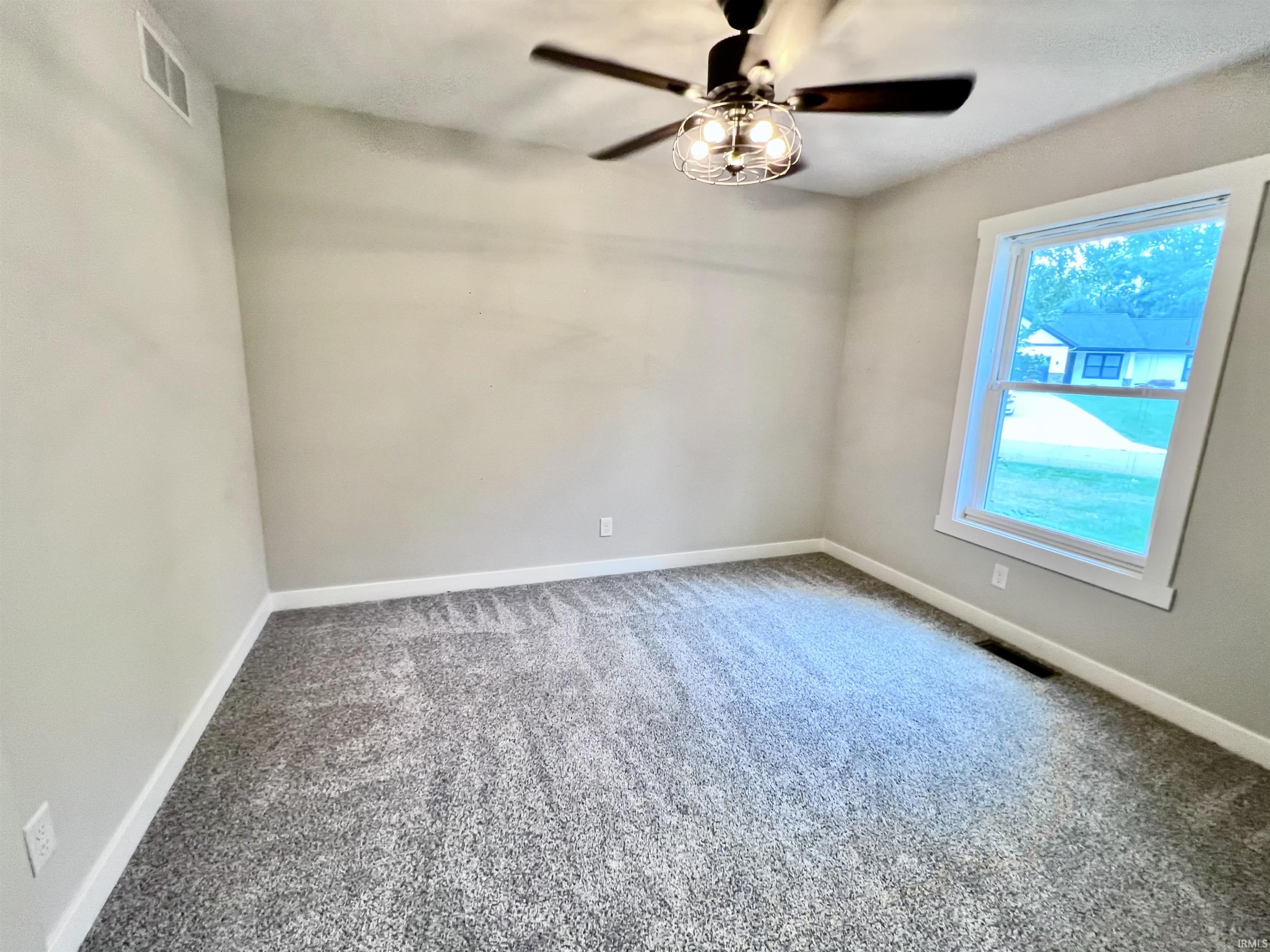 Bright bedroom featuring neutral wall finishes, carpet flooring, a ceiling fan with integrated lighting fixture, and a large window allowing natural light