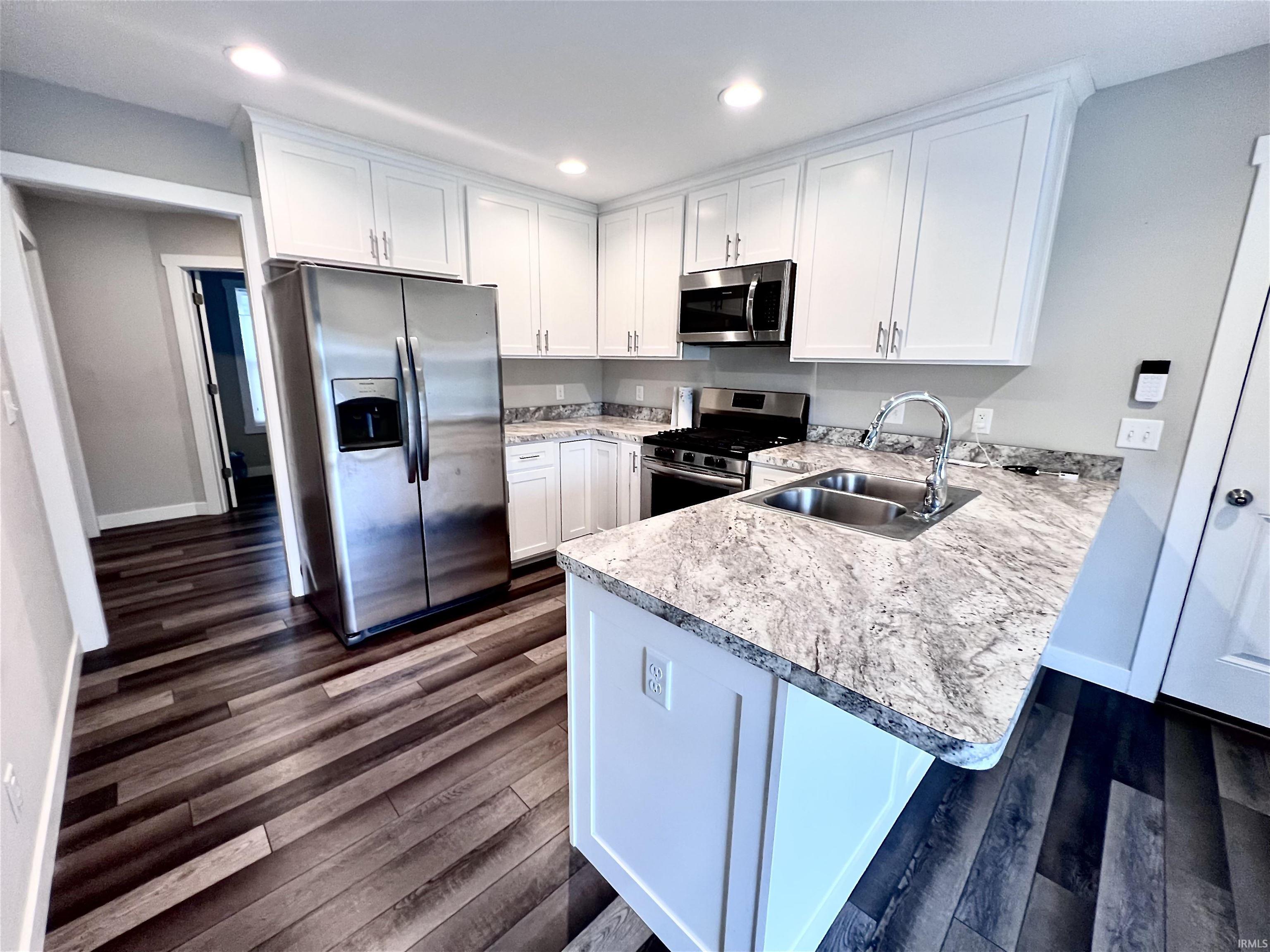 Modern kitchen featuring white cabinetry, stainless steel appliances, and a large island with engineered stone countertops