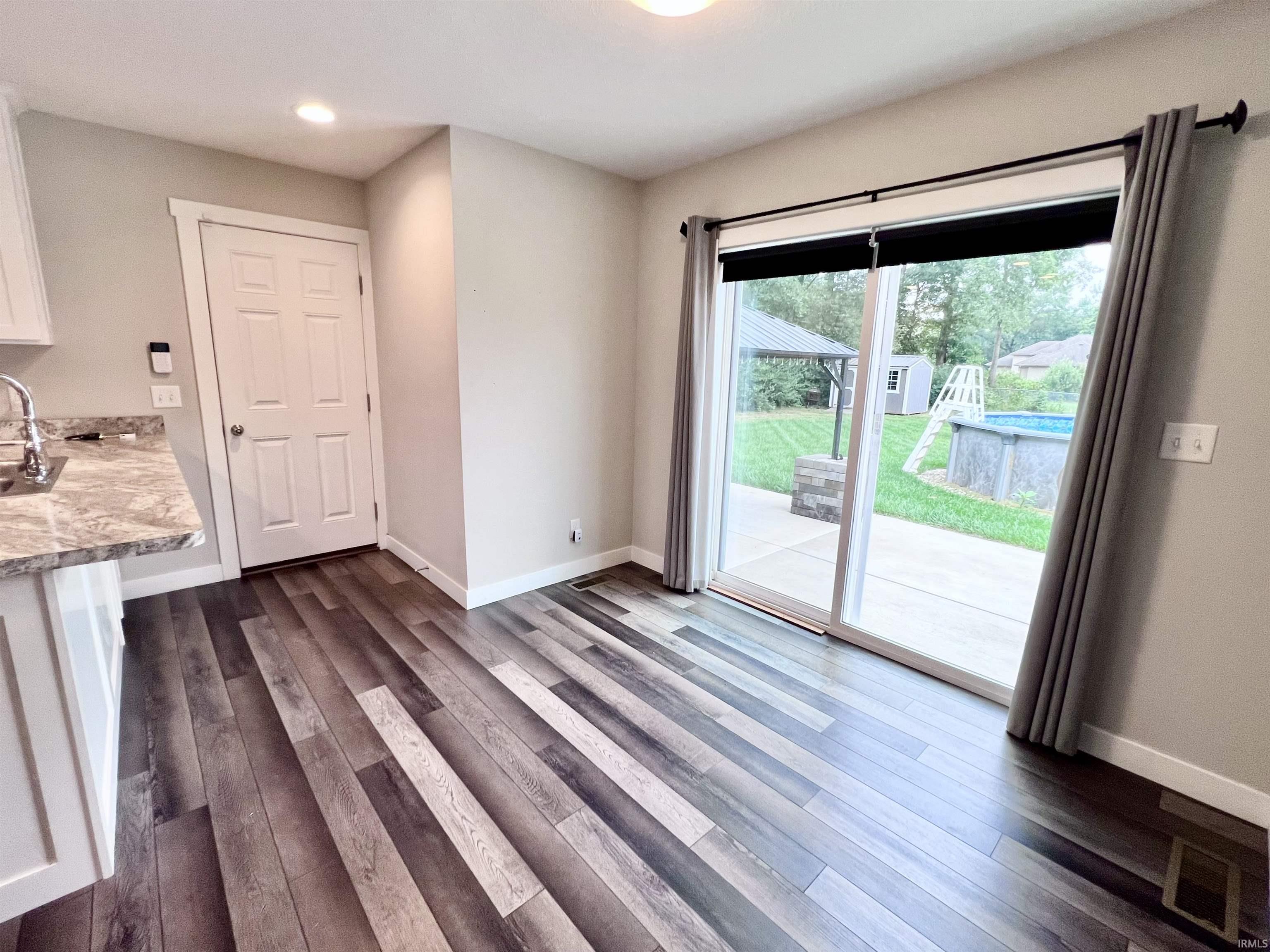 Wood-finish flooring, white cabinetry, granite-look countertop, stainless steel sink with a gooseneck faucet, and a sliding glass door