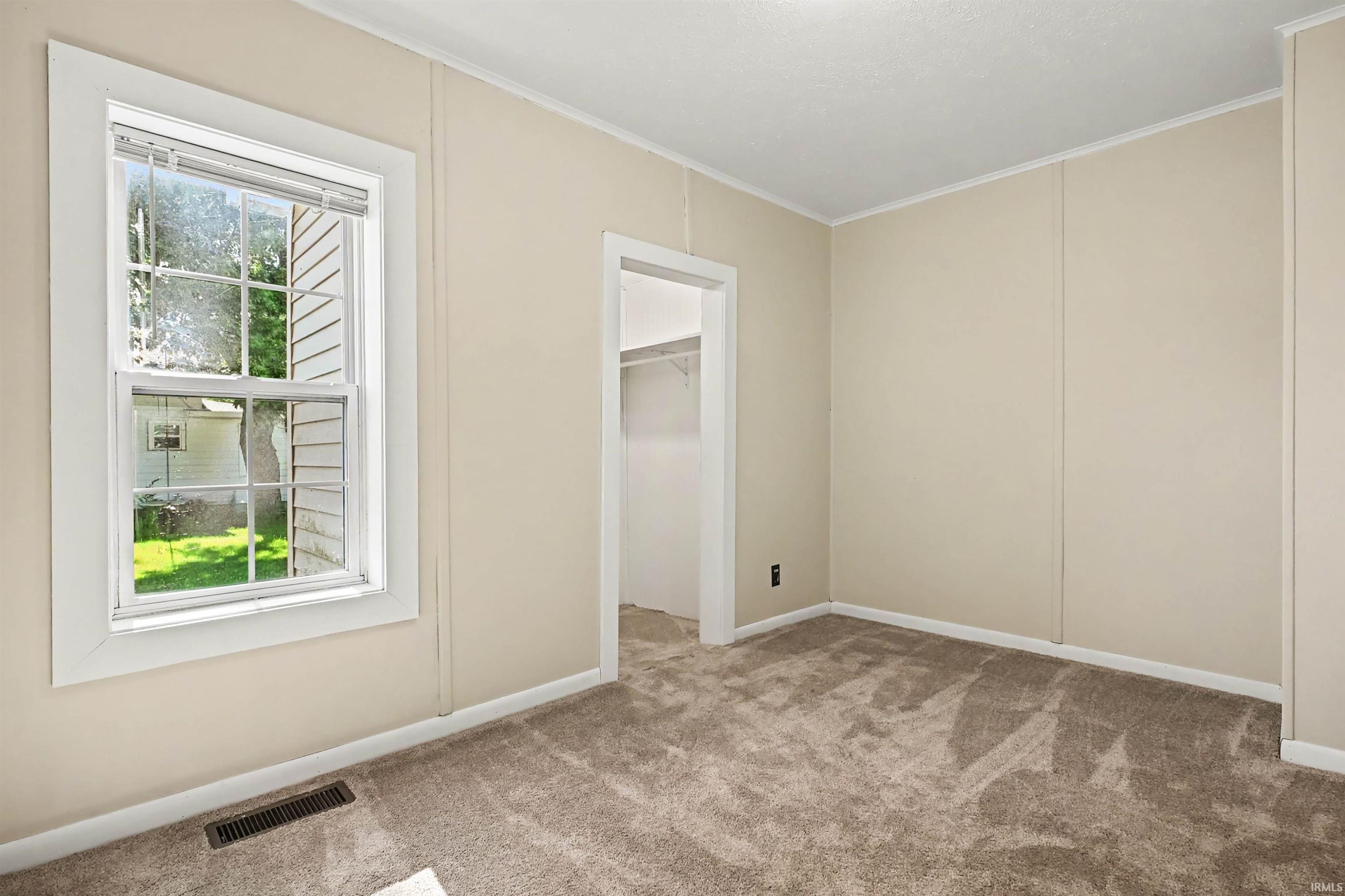 Neutral-toned room featuring a double-hung window, light beige wall paneling, white trim details, and plush carpeting