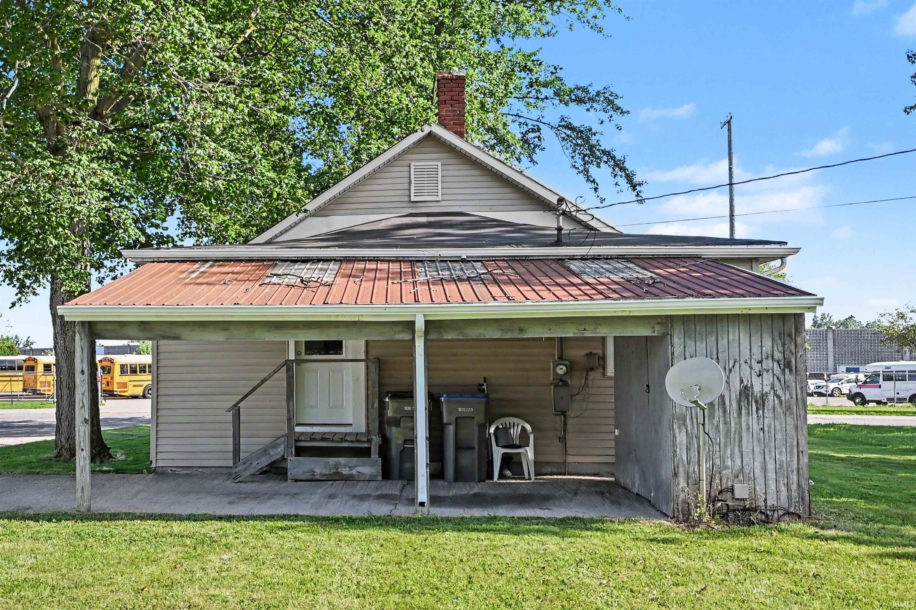 Rear exterior featuring a covered porch, vinyl siding, a red metal roof, and a red brick chimney