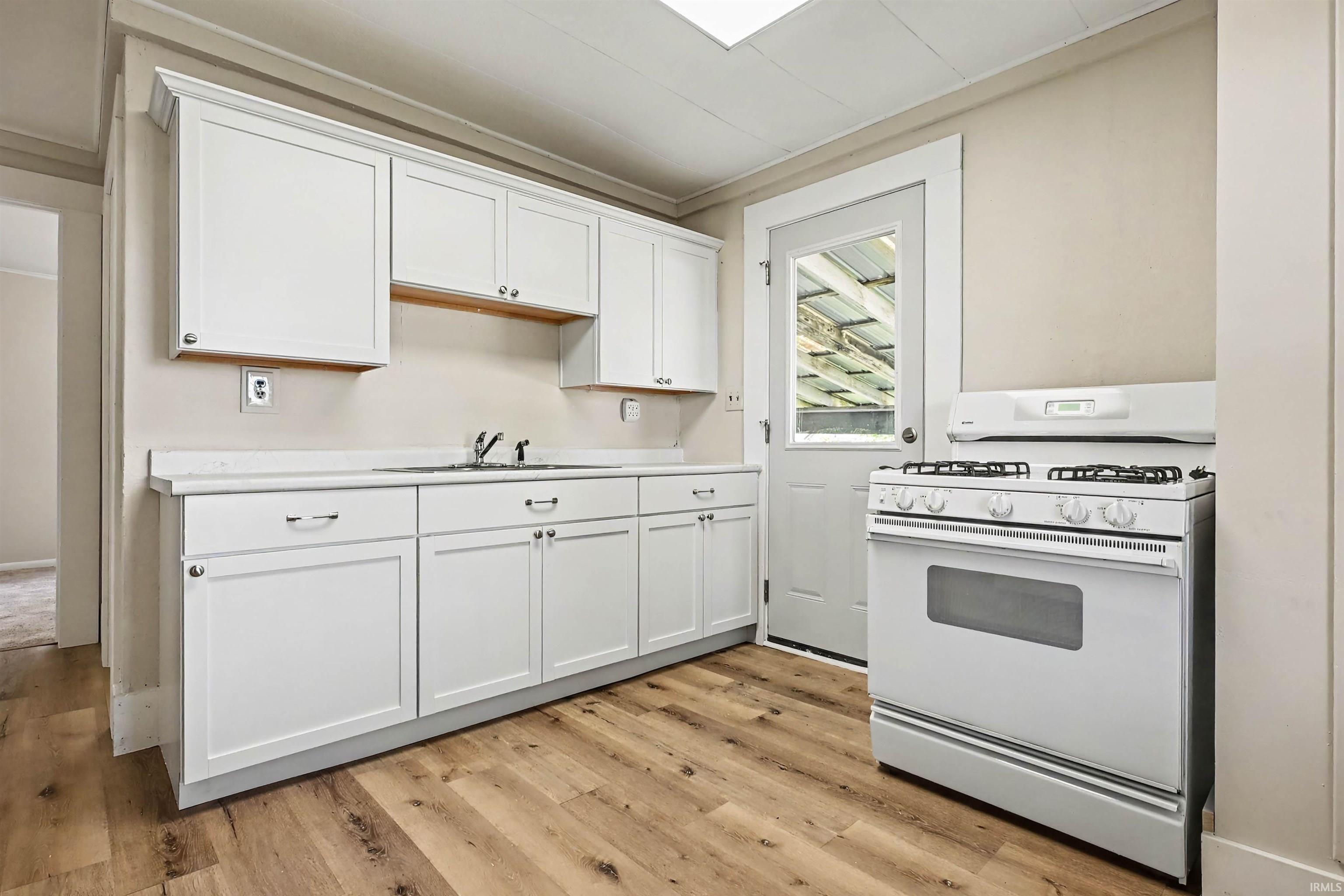 Kitchen featuring abundant white cabinetry, light-toned countertops, wood-finish flooring, a stainless steel sink, and a white freestanding range