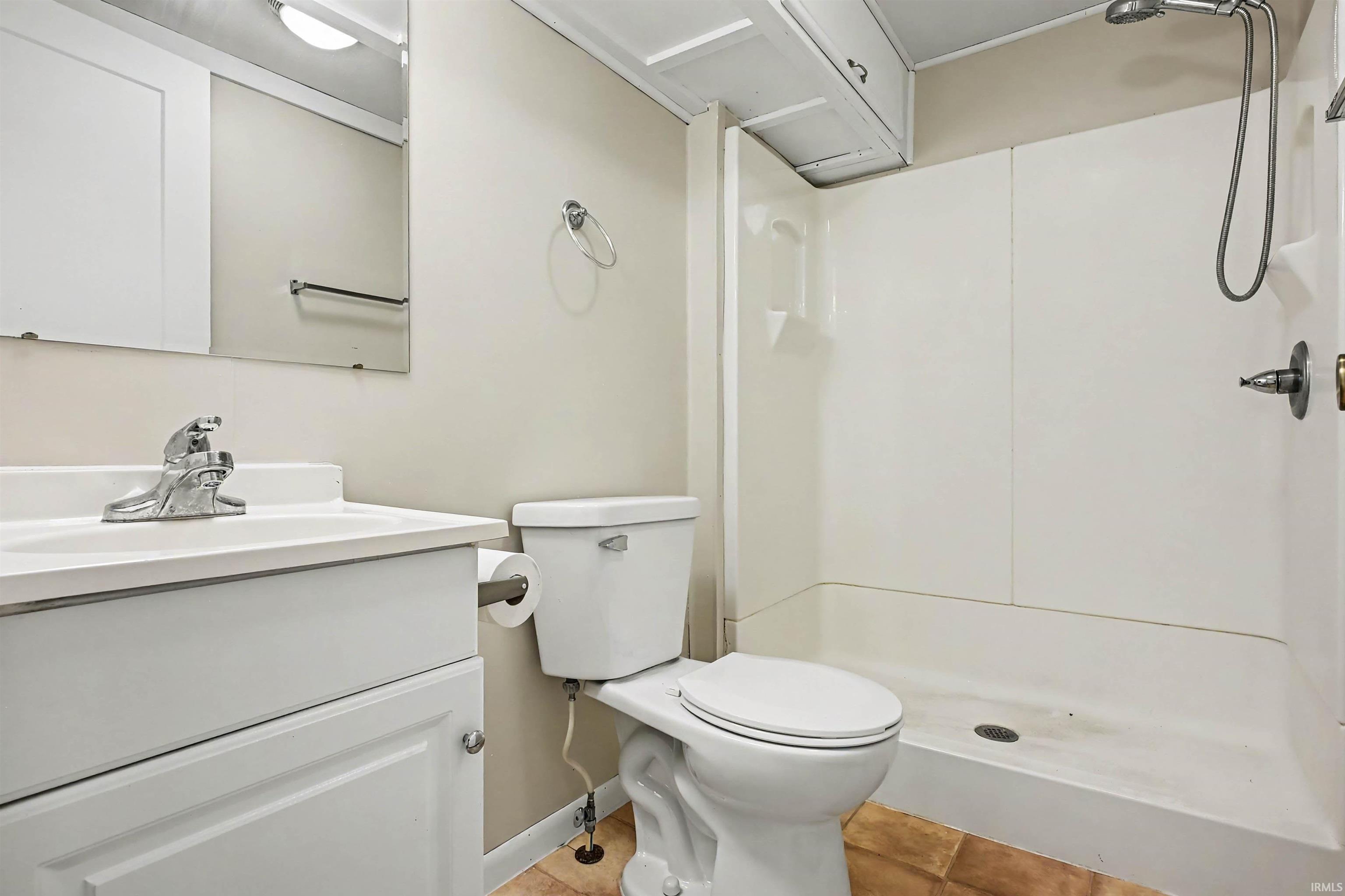 Bathroom featuring a white vanity with a single basin sink, mirror, toilet, and a stand-up shower with a handheld fixture