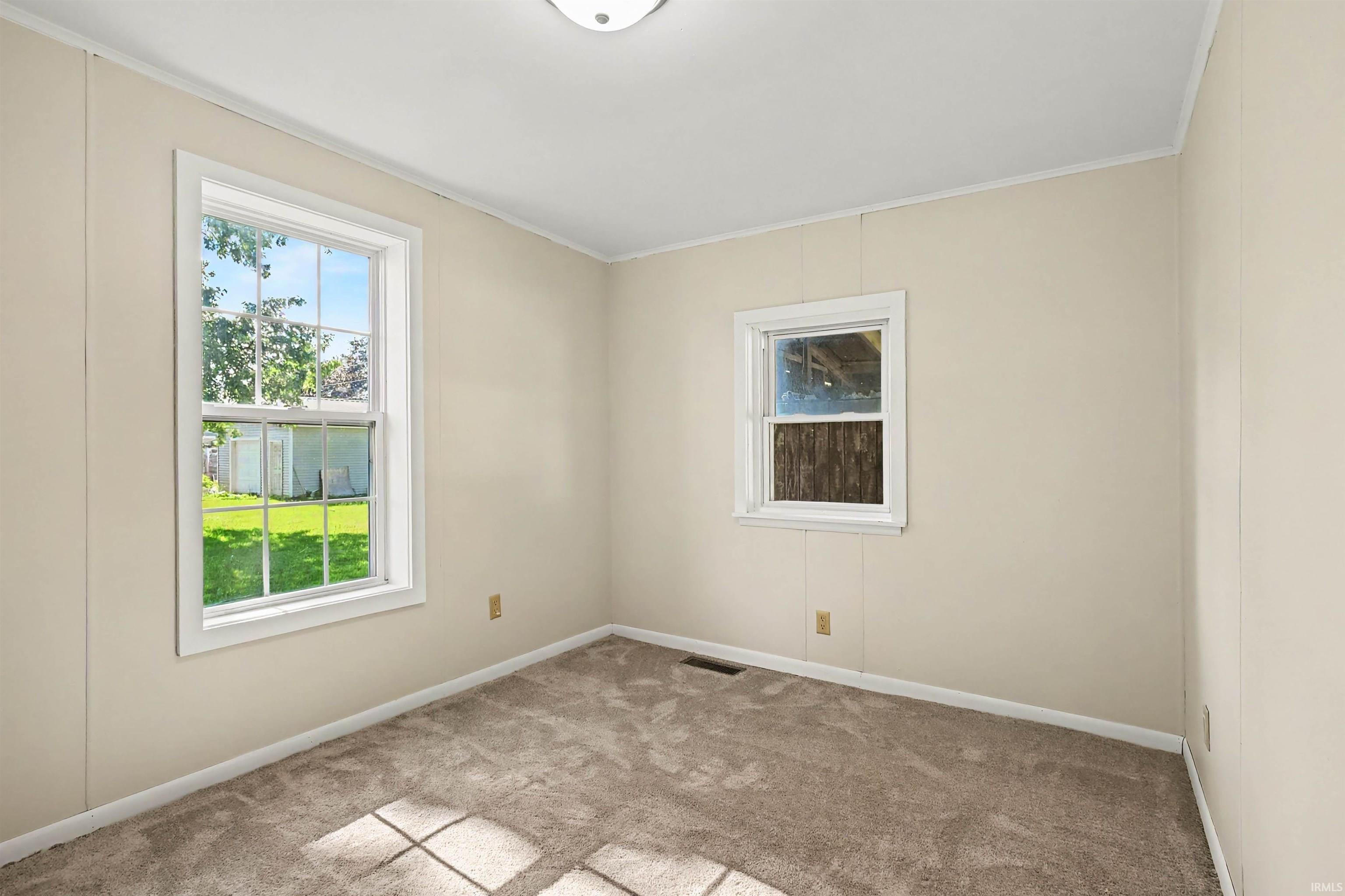 Two double-hung windows with white trim, light beige wall paneling, light brown carpeting, white baseboards, and a flush mount ceiling light