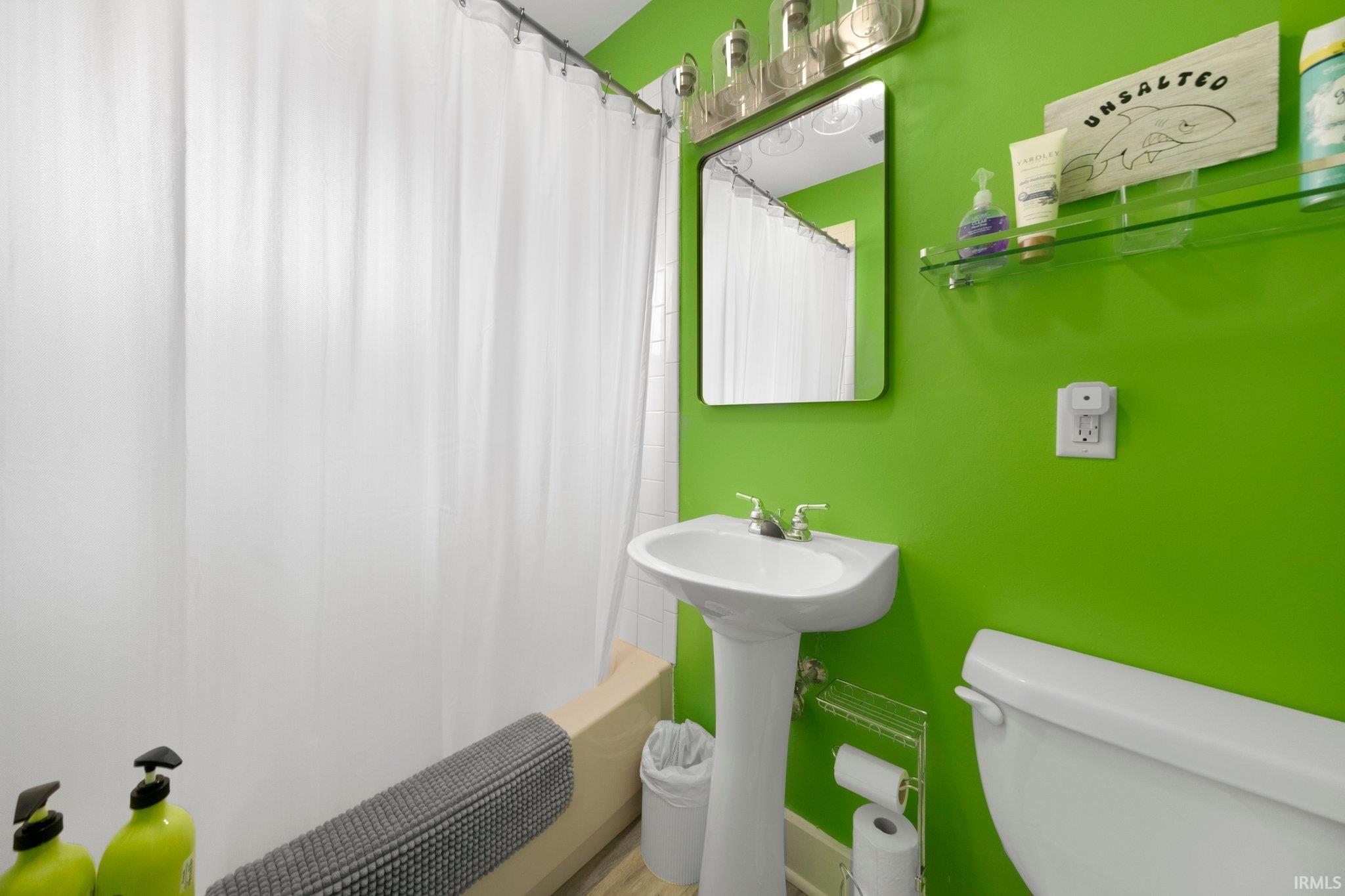 Bathroom featuring a pedestal sink with chrome fixtures, a rectangular vanity mirror, and a wall-mounted light fixture
