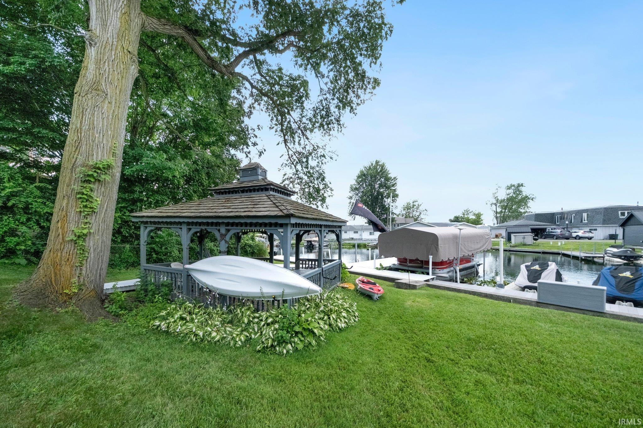 Waterfront property featuring a wood gazebo with a shingled roof, a mature tree, a manicured lawn, and boat docks