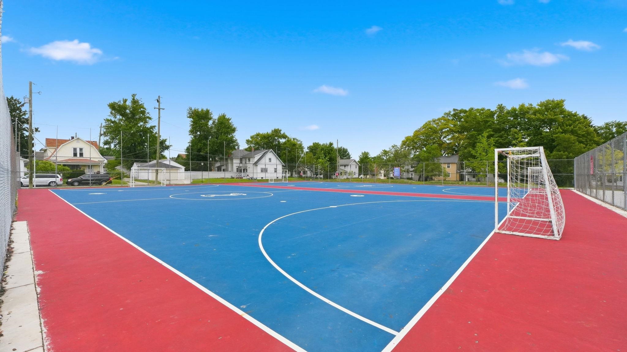 Multi-sport court featuring vibrant red and blue surfacing, white court line markings, and a perimeter fence