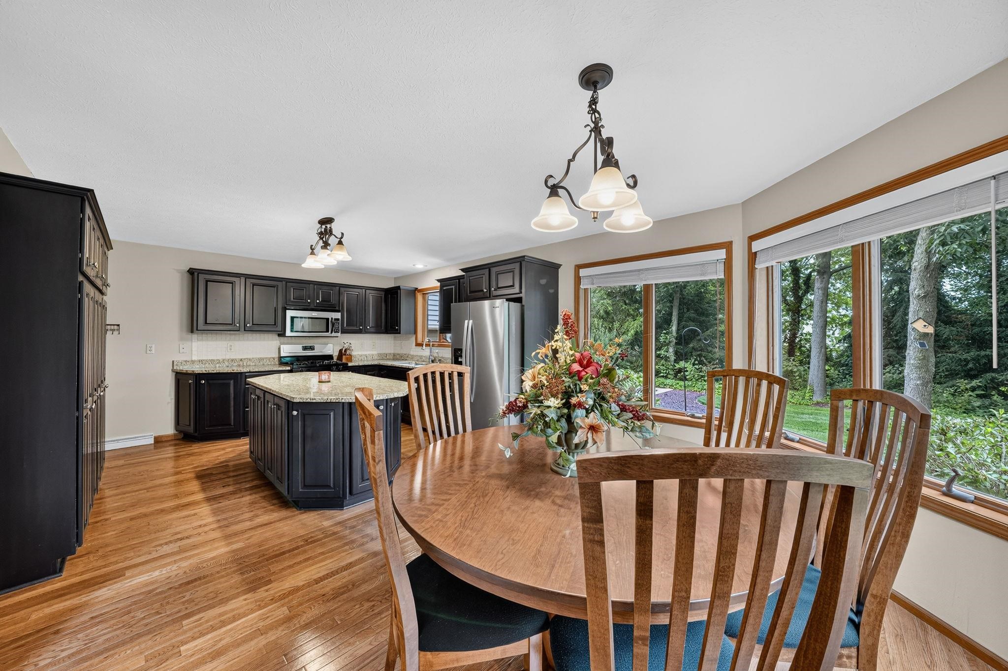 Kitchen and dining area featuring wood-finish flooring, dark cabinetry, a kitchen island with a light-colored countertop, and stainless steel appliances