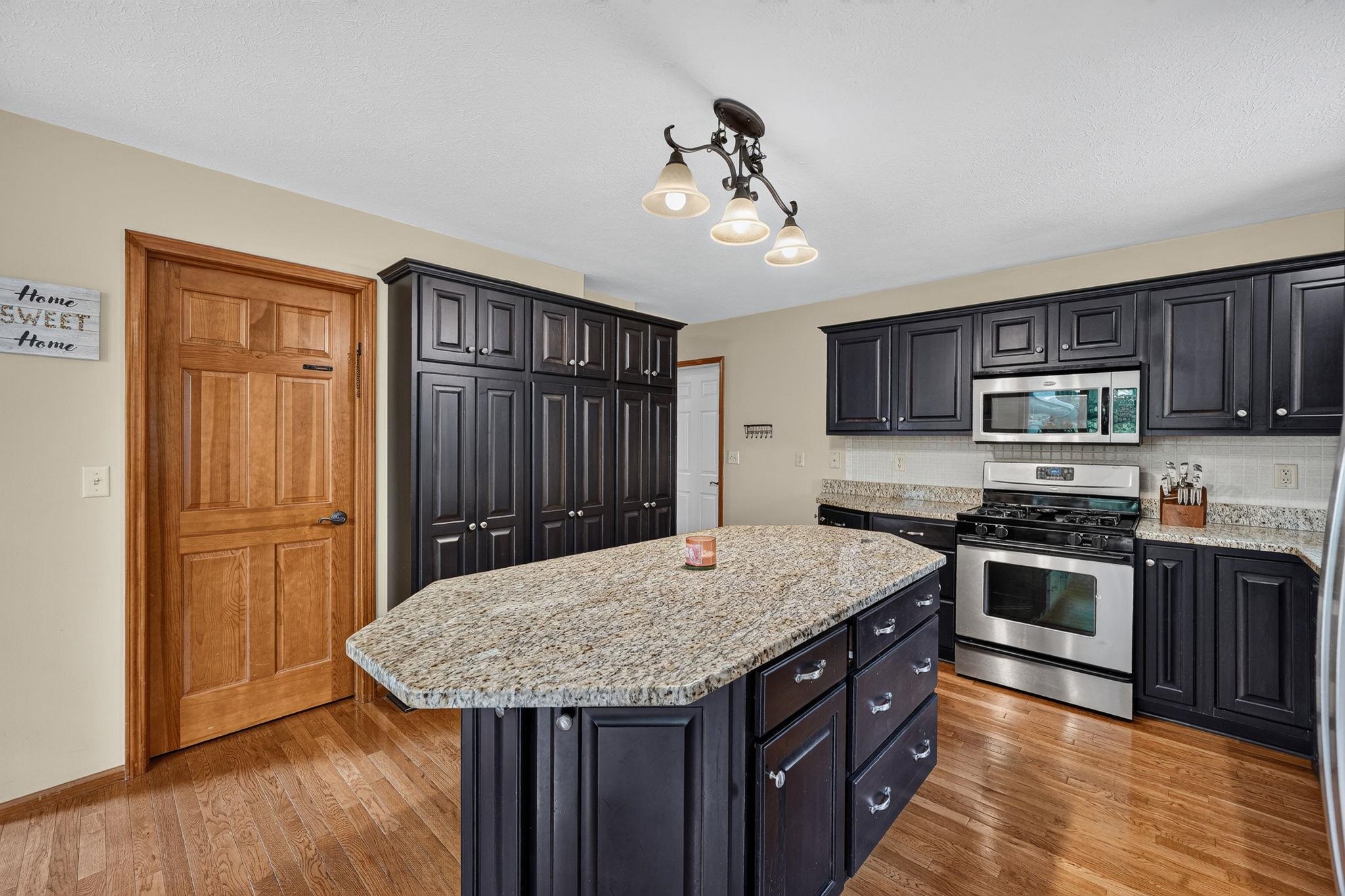Kitchen featuring an expansive center island with a light-toned countertop, dark wood-finish cabinetry, stainless steel appliances, wood-finish flooring, and a multi-light ceiling fixture