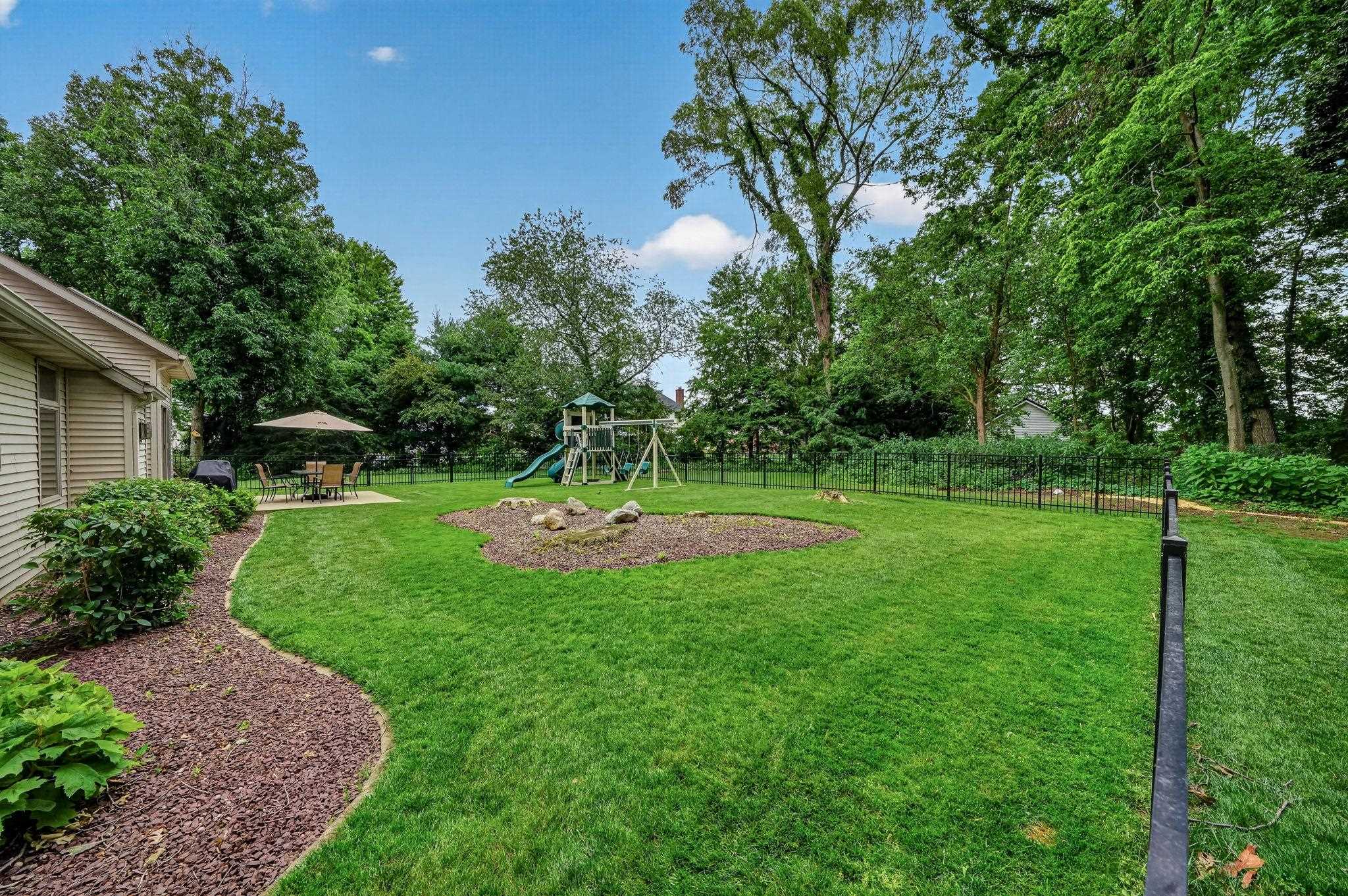 Expansive backyard featuring a manicured lawn, paved patio, and mature perimeter trees