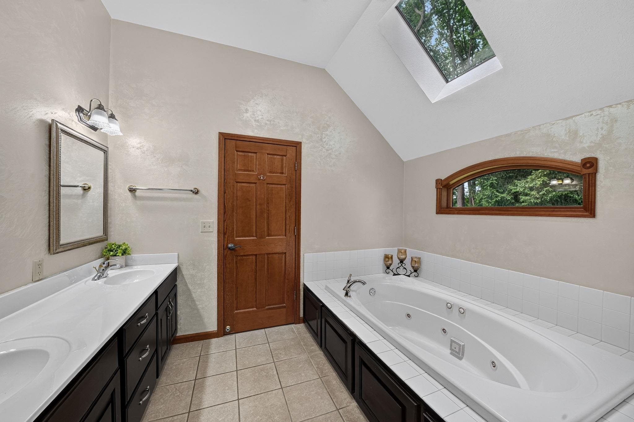 Bathroom featuring a dual vanity with undermount sinks, a built-in jetted tub, a skylight, and a vaulted ceiling
