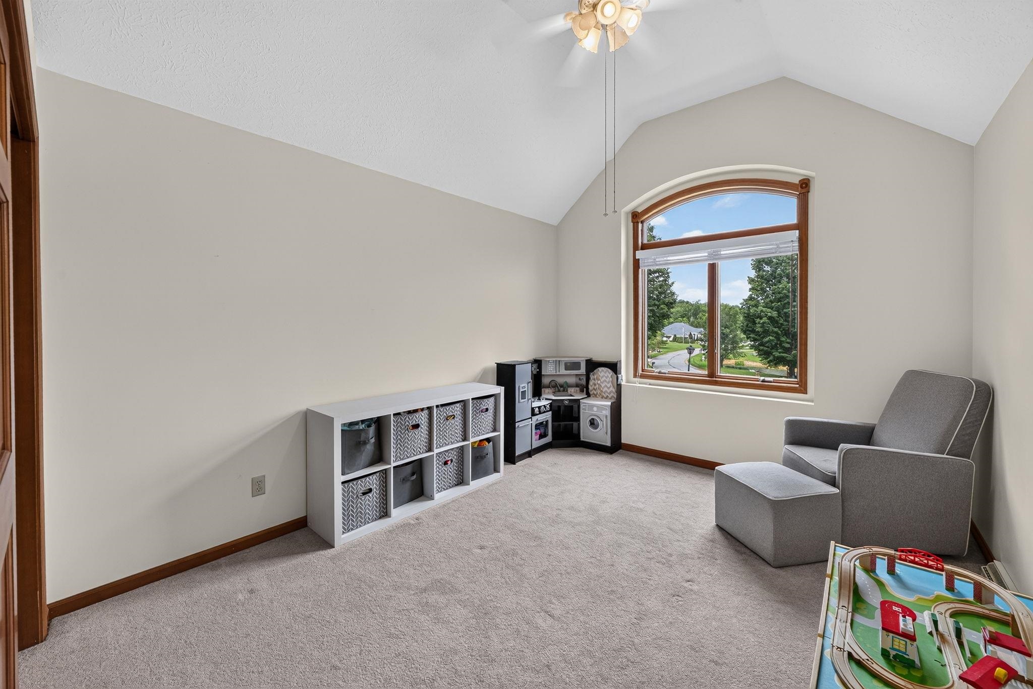 Vaulted ceiling room featuring an arched window with wood-finish trim, light-toned carpeting, and a ceiling fan