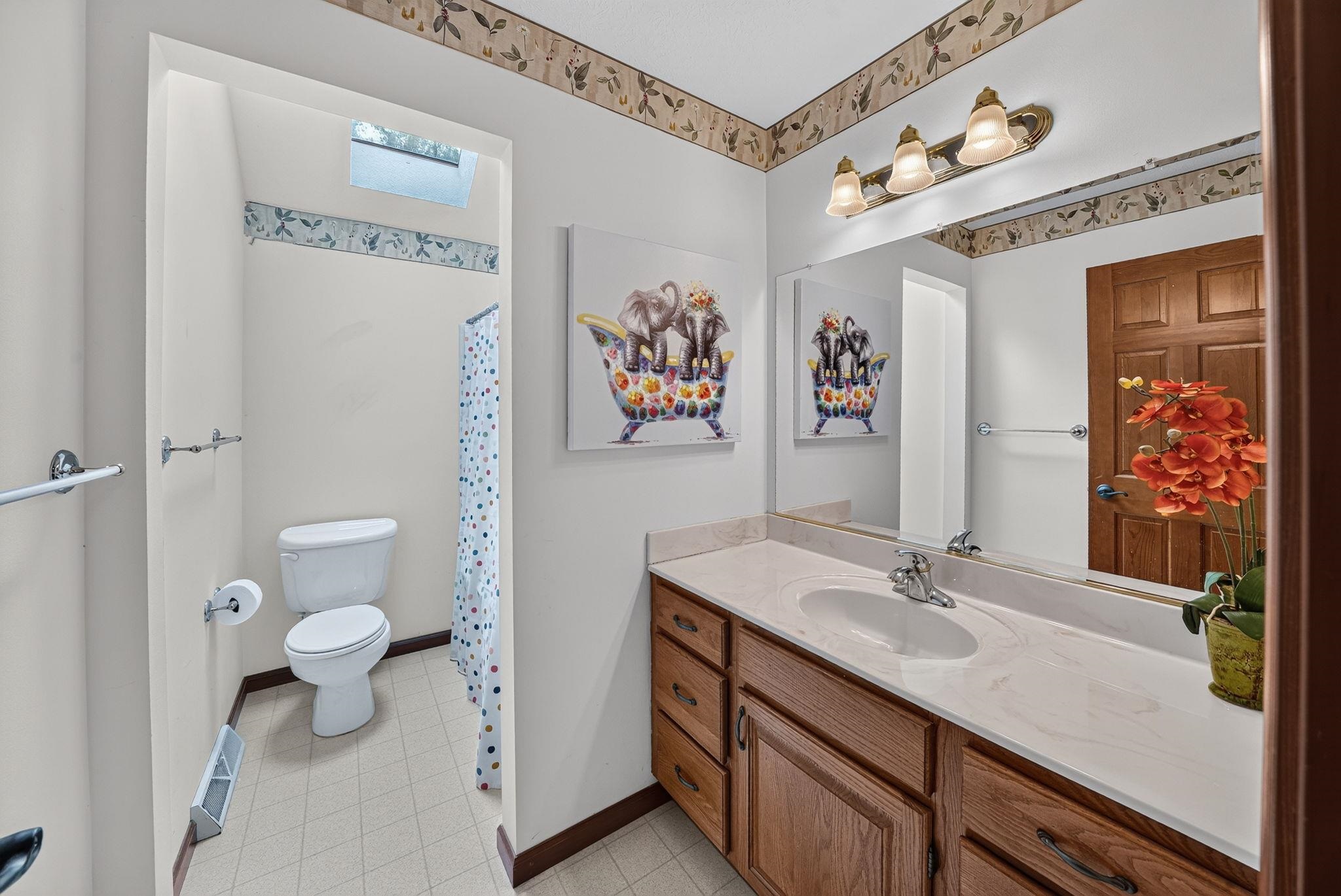 Bathroom featuring a wood-finish vanity with an integrated sink, a full-width wall mirror, and a three-light fixture