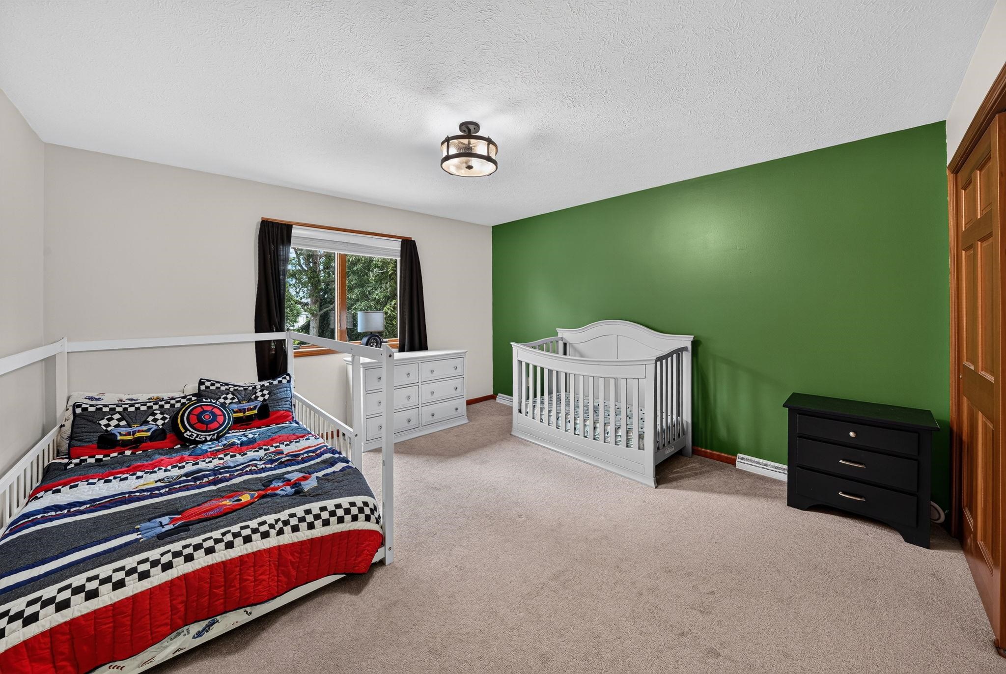 Carpeted room with a green accent wall, light-colored walls, and a window with black drapes
