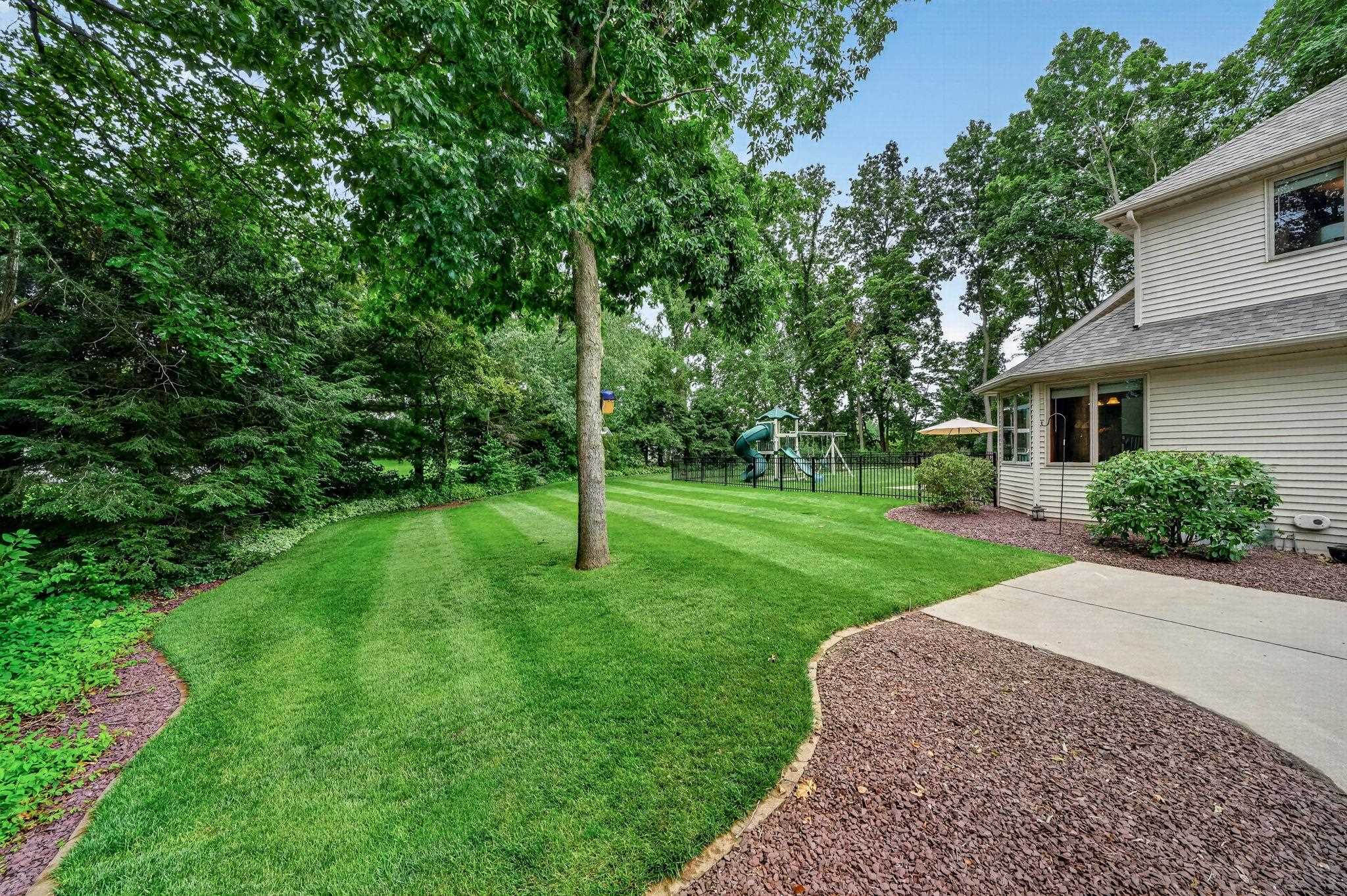 Expansive rear yard featuring a wide concrete walkway, mature trees, and a substantial lawn area