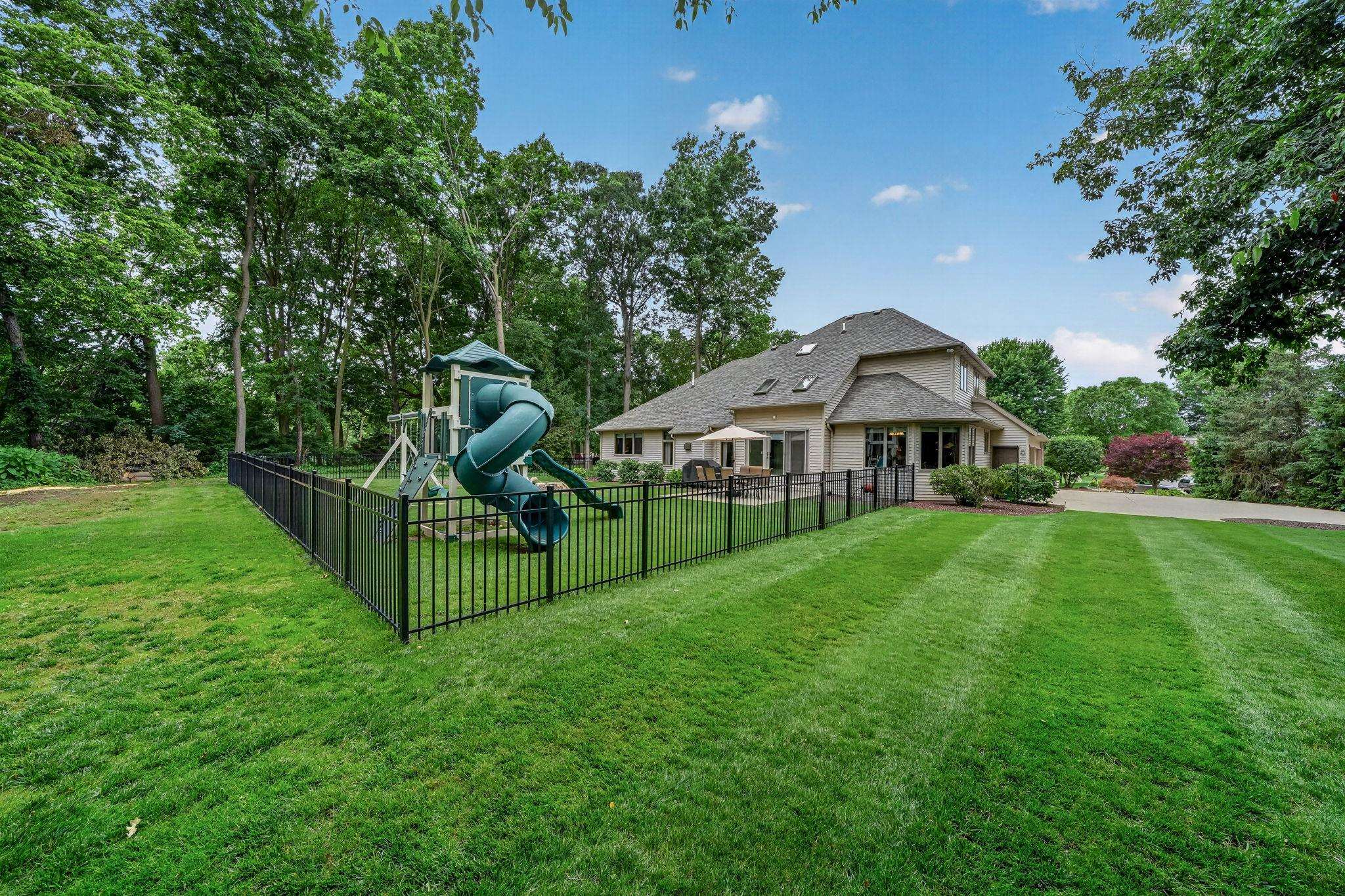 Expansive green lawn with mature trees and a black iron fence