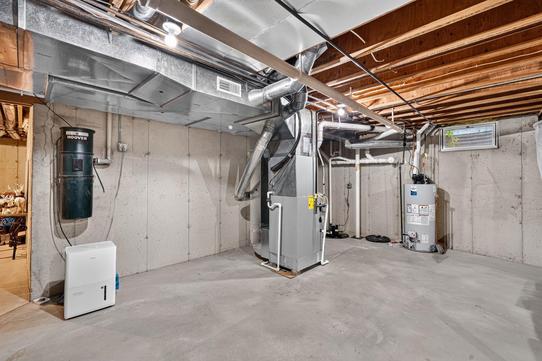 Unfinished concrete basement featuring exposed joists, concrete block walls, and a dedicated utility area