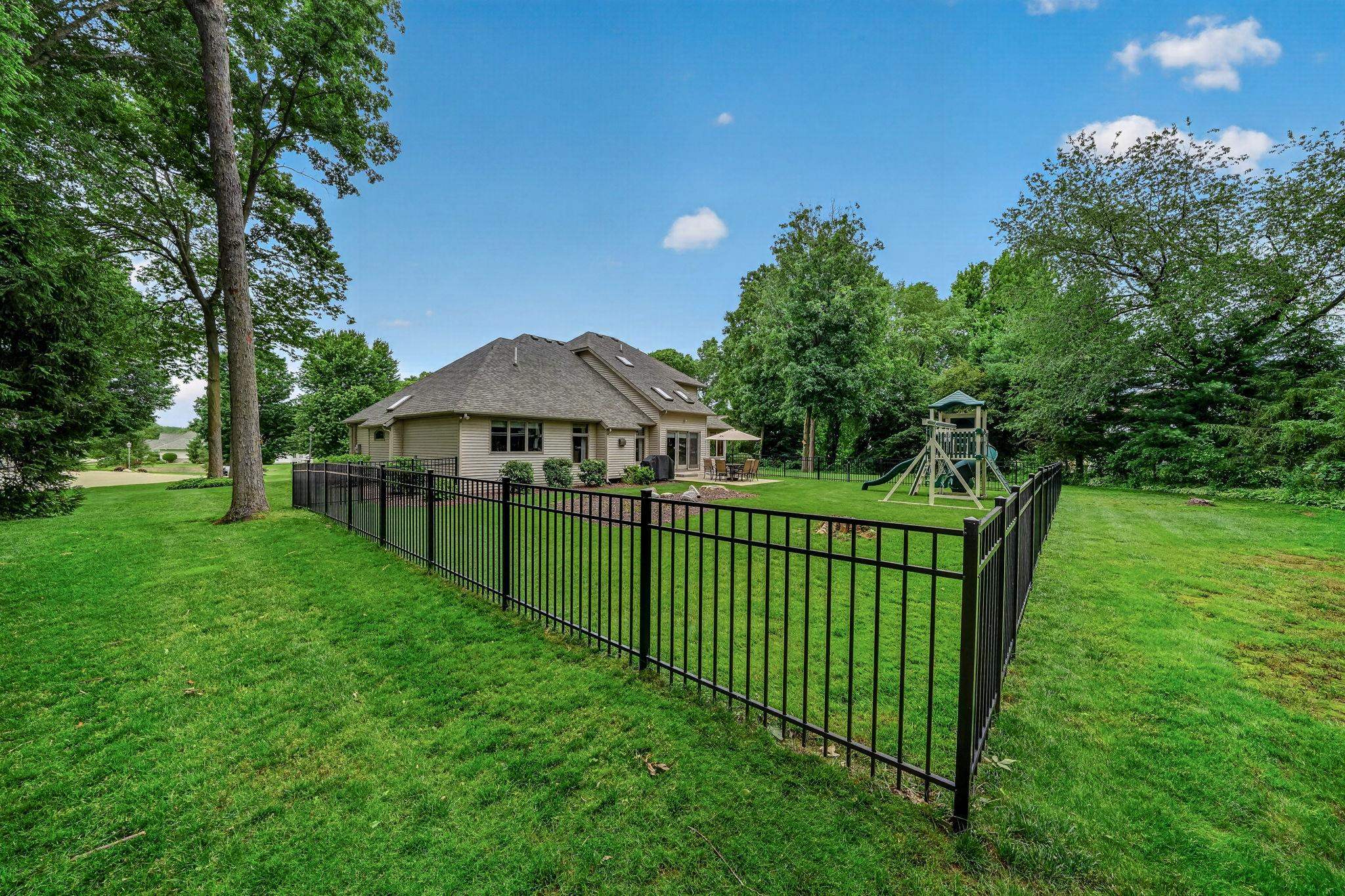 Expansive fenced-in backyard featuring a manicured lawn, mature trees, and a beige stucco exterior