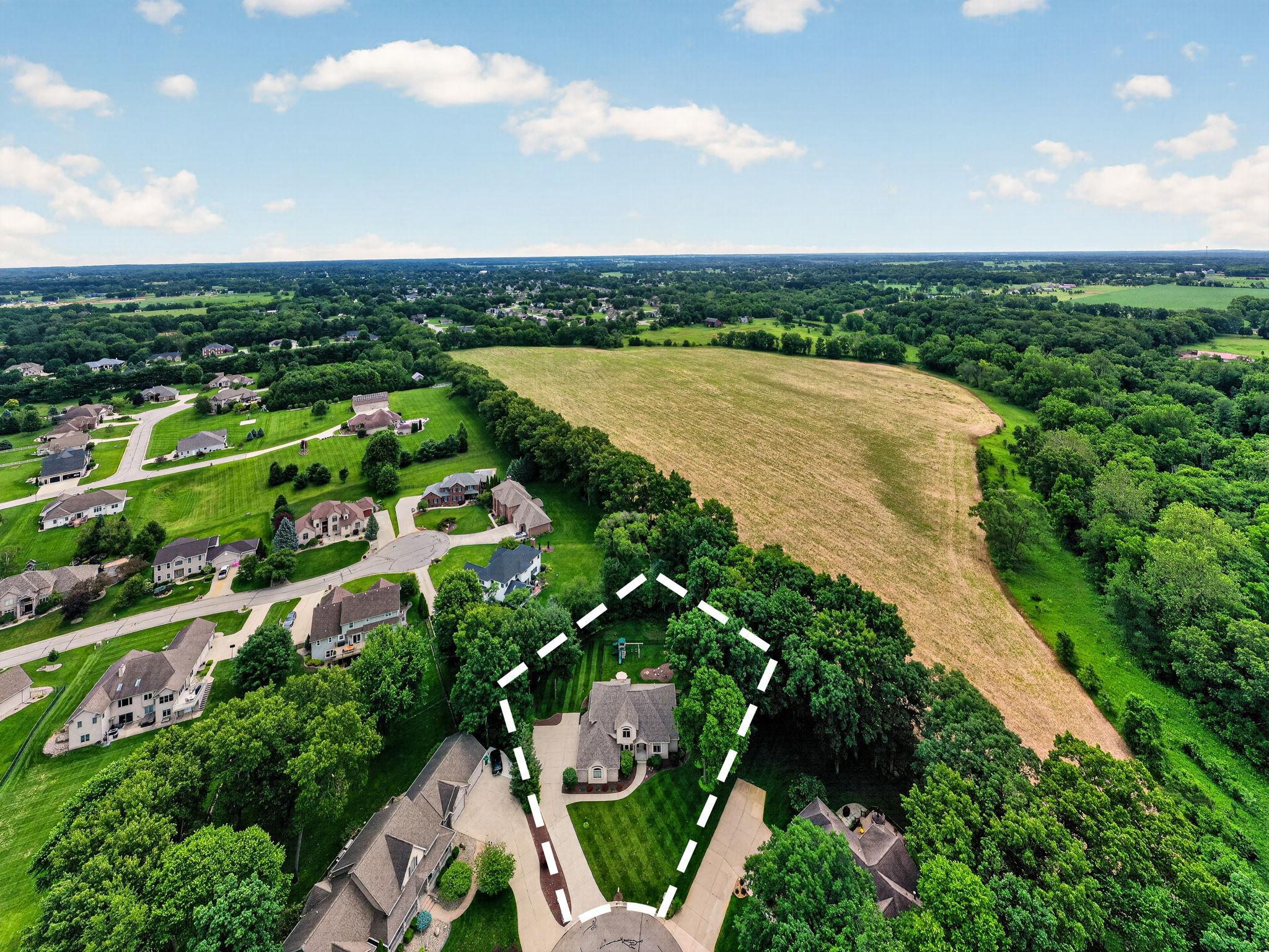 Aerial view highlighting the property's expansive lot, bordered by mature trees and open fields