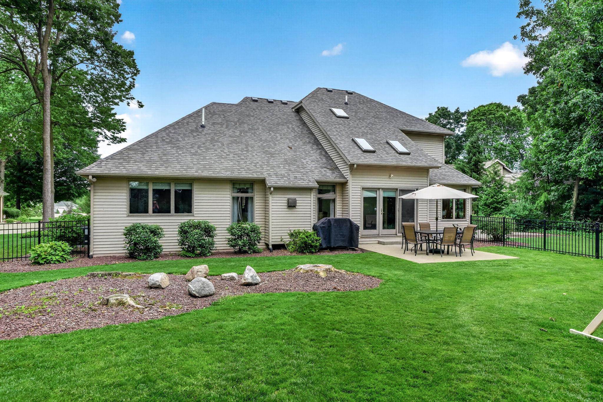 Expansive rear yard featuring a concrete patio, perimeter fencing, mature trees, and landscaping elements