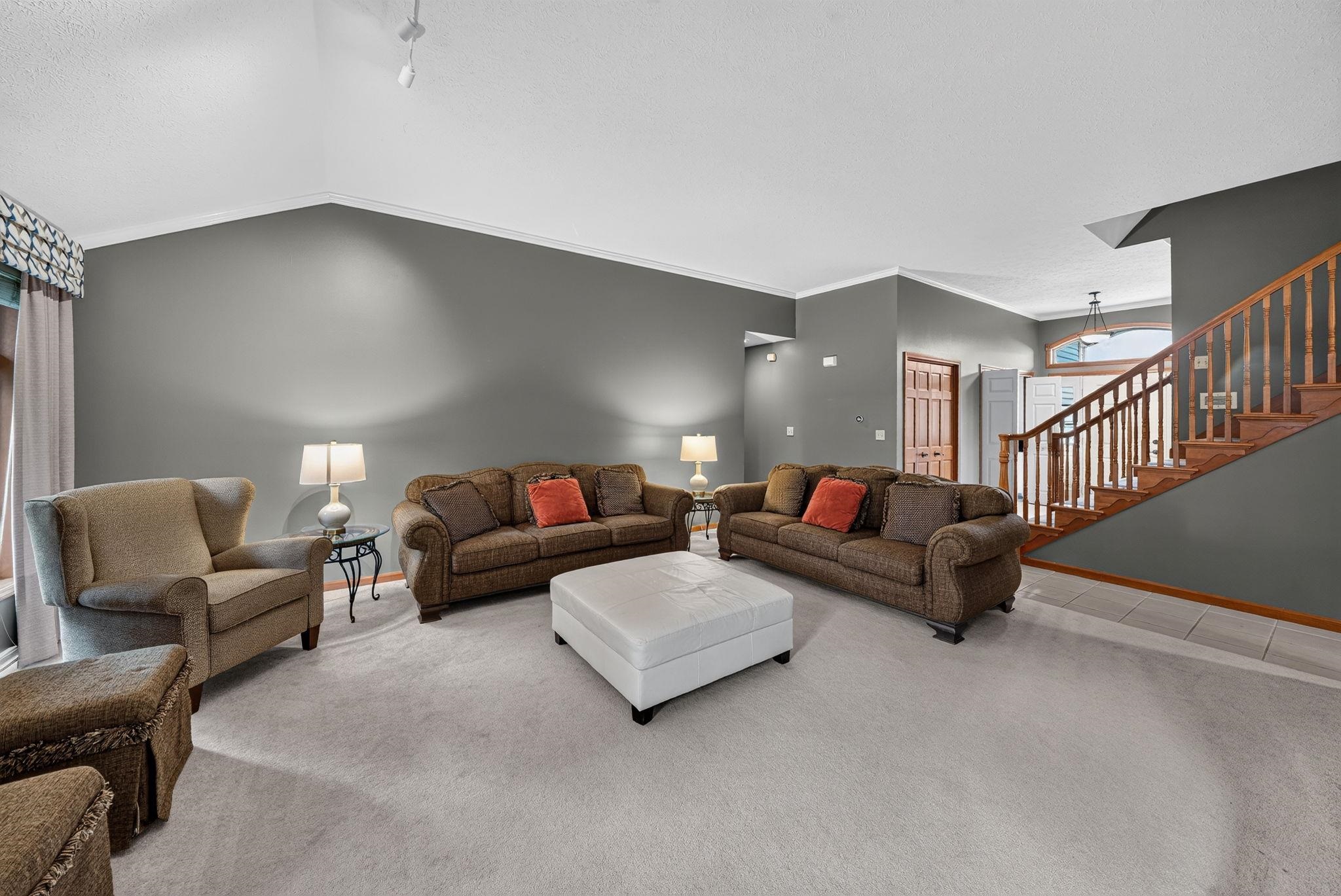 Living area featuring vaulted ceilings, light-toned carpeting, and a wooden staircase with balusters