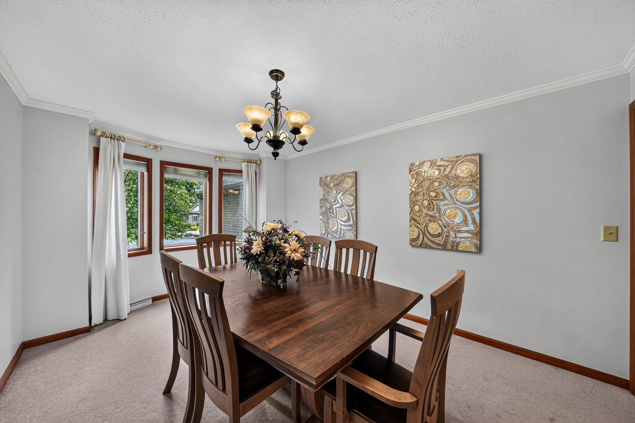 Dining area featuring a classic chandelier, a bay window with wood trim, crown molding, and carpeted flooring