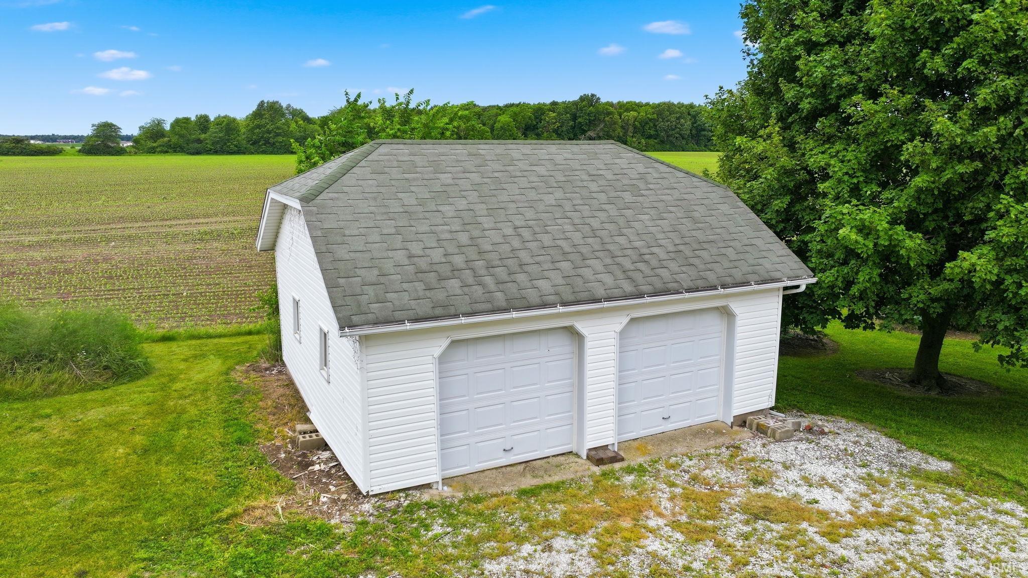 Two-car detached garage with white siding and a gray shingle roof, set on a concrete foundation with a gravel apron