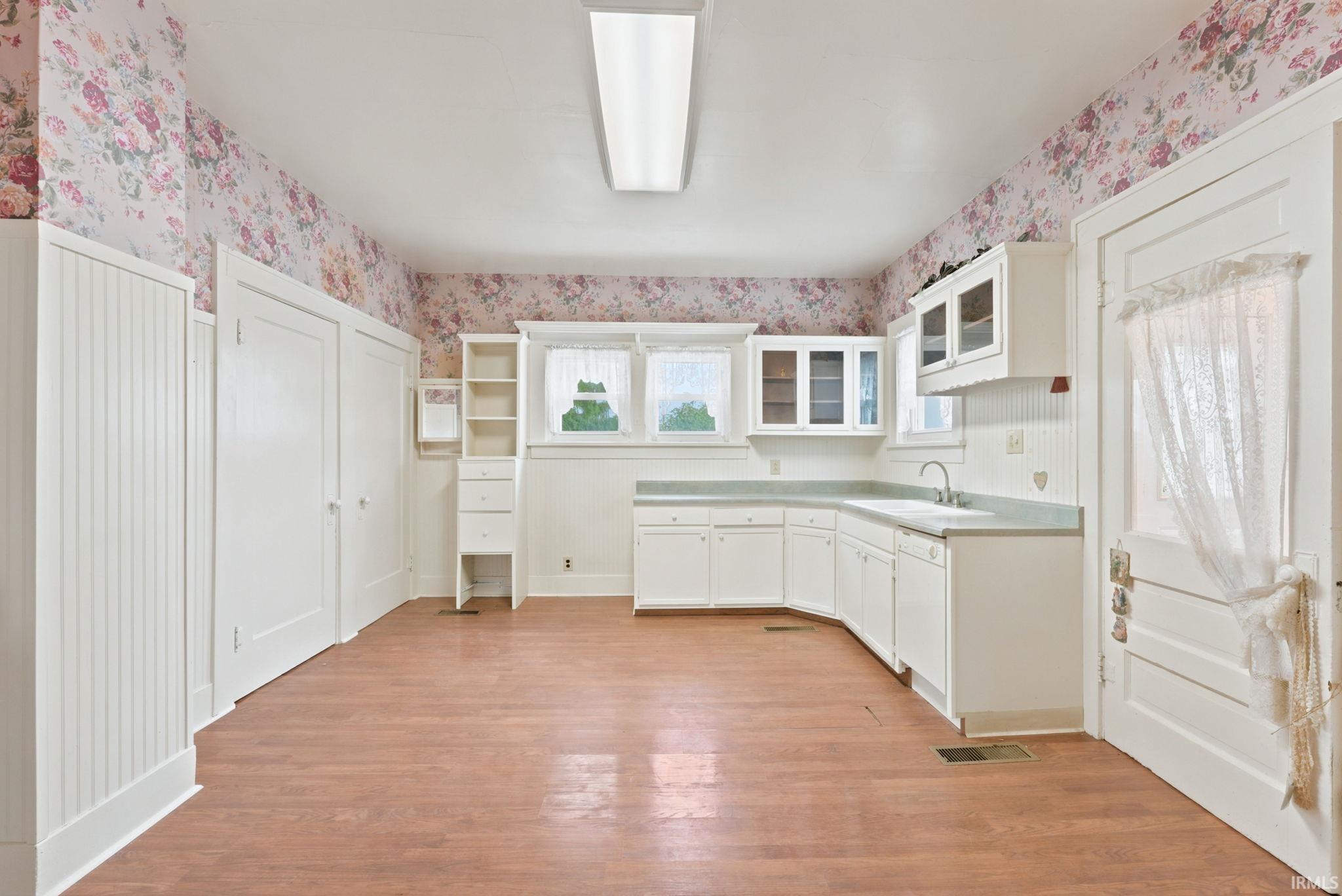 Spacious room featuring wood-finish flooring, floral wallpaper, and white beadboard paneling