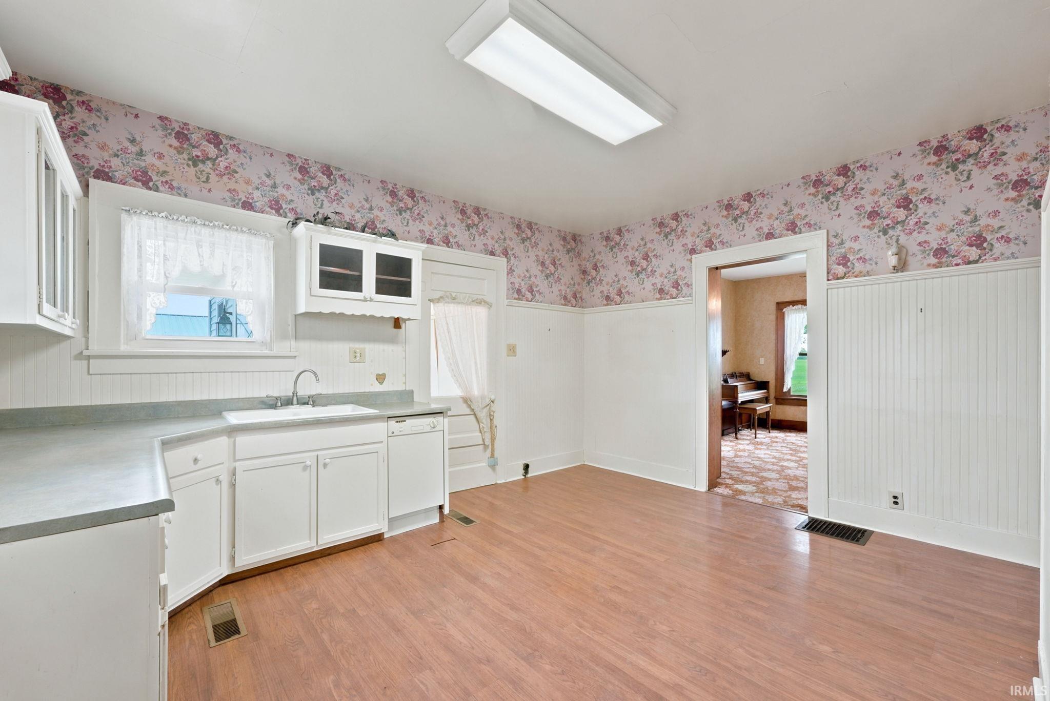 Kitchen featuring wood-finish flooring, white cabinetry, a sink, and an integrated dishwasher