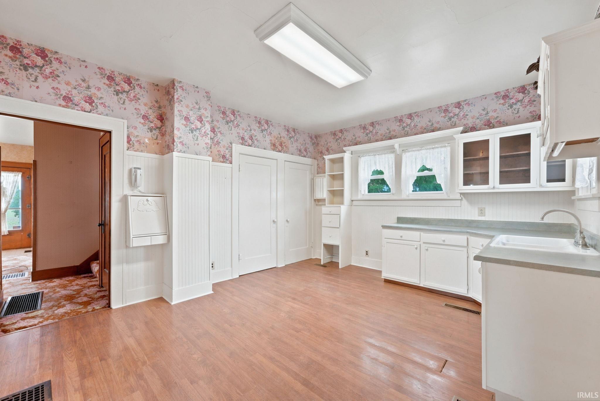 Kitchen area featuring wood-finish flooring, white cabinetry, a built-in sink, and windows with natural light