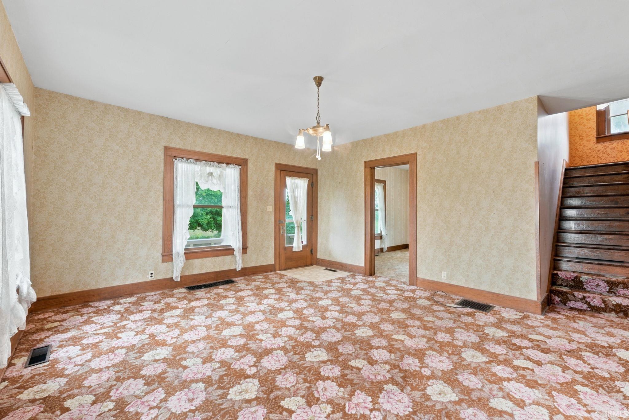 Spacious interior room featuring patterned carpeting, wallpapered walls, and substantial wood trim