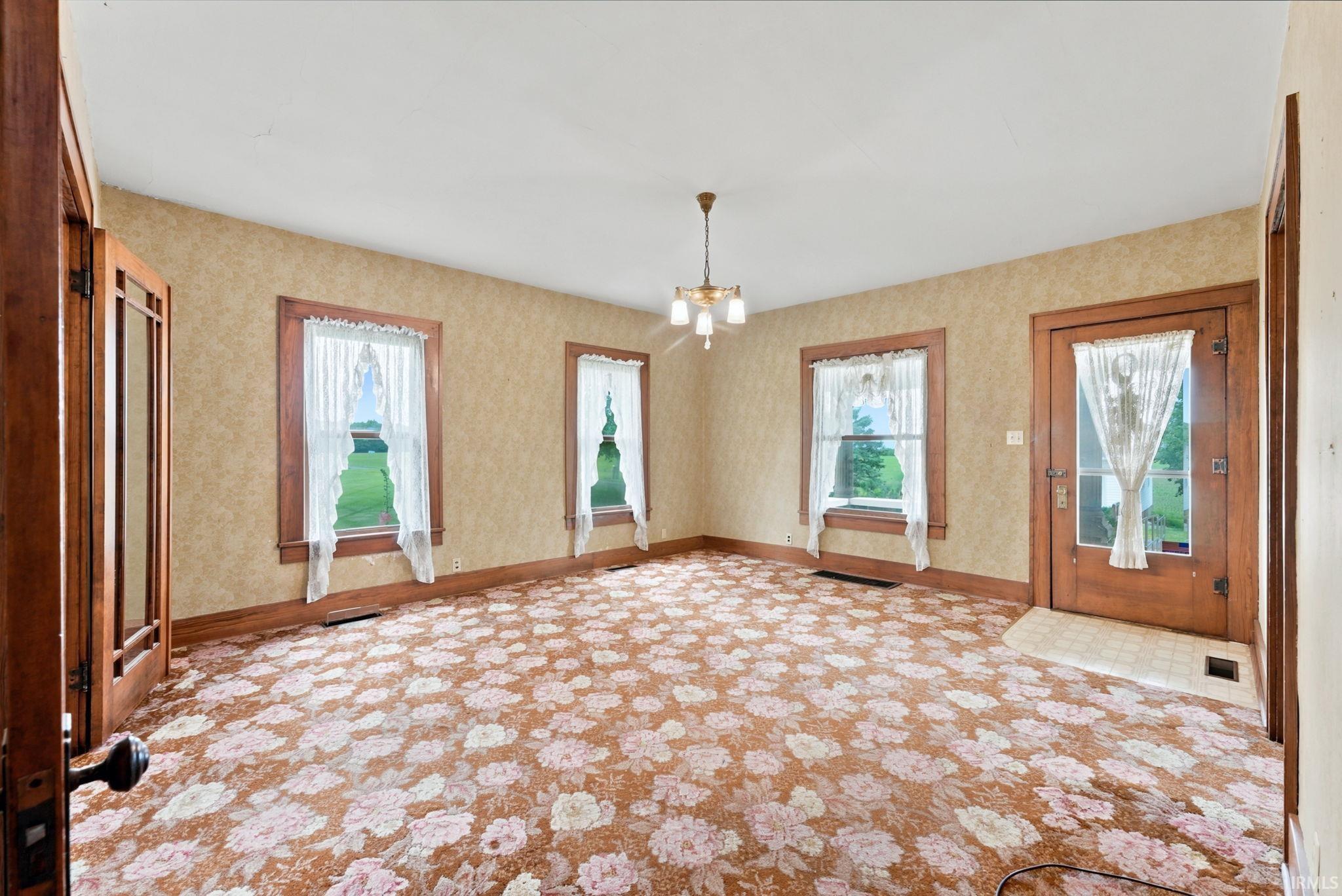 Room featuring patterned carpet, multiple windows with natural light, wood trim, and a ceiling-mounted light fixture