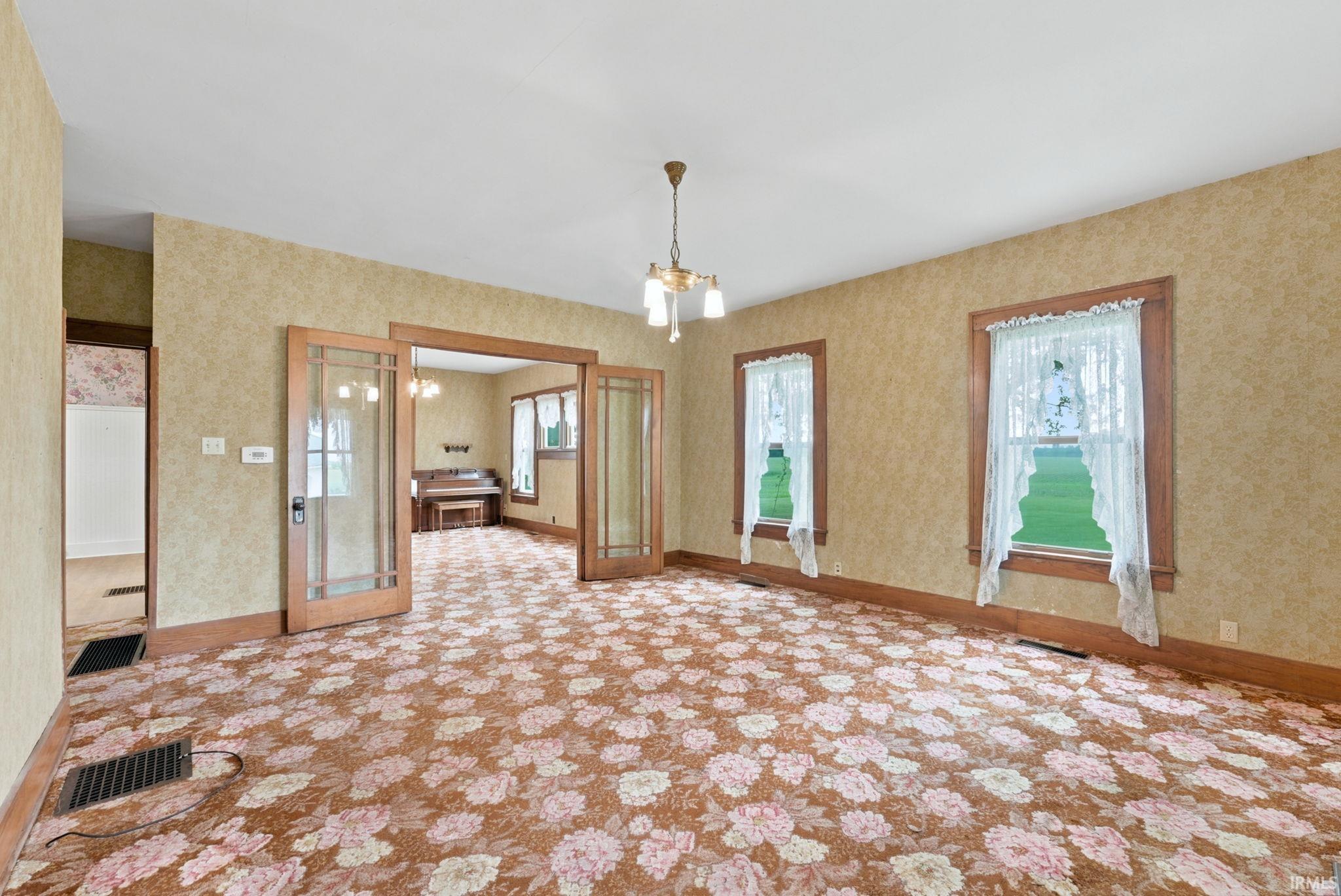 Spacious room featuring patterned carpet flooring, wallpapered walls, and two windows with wood trim