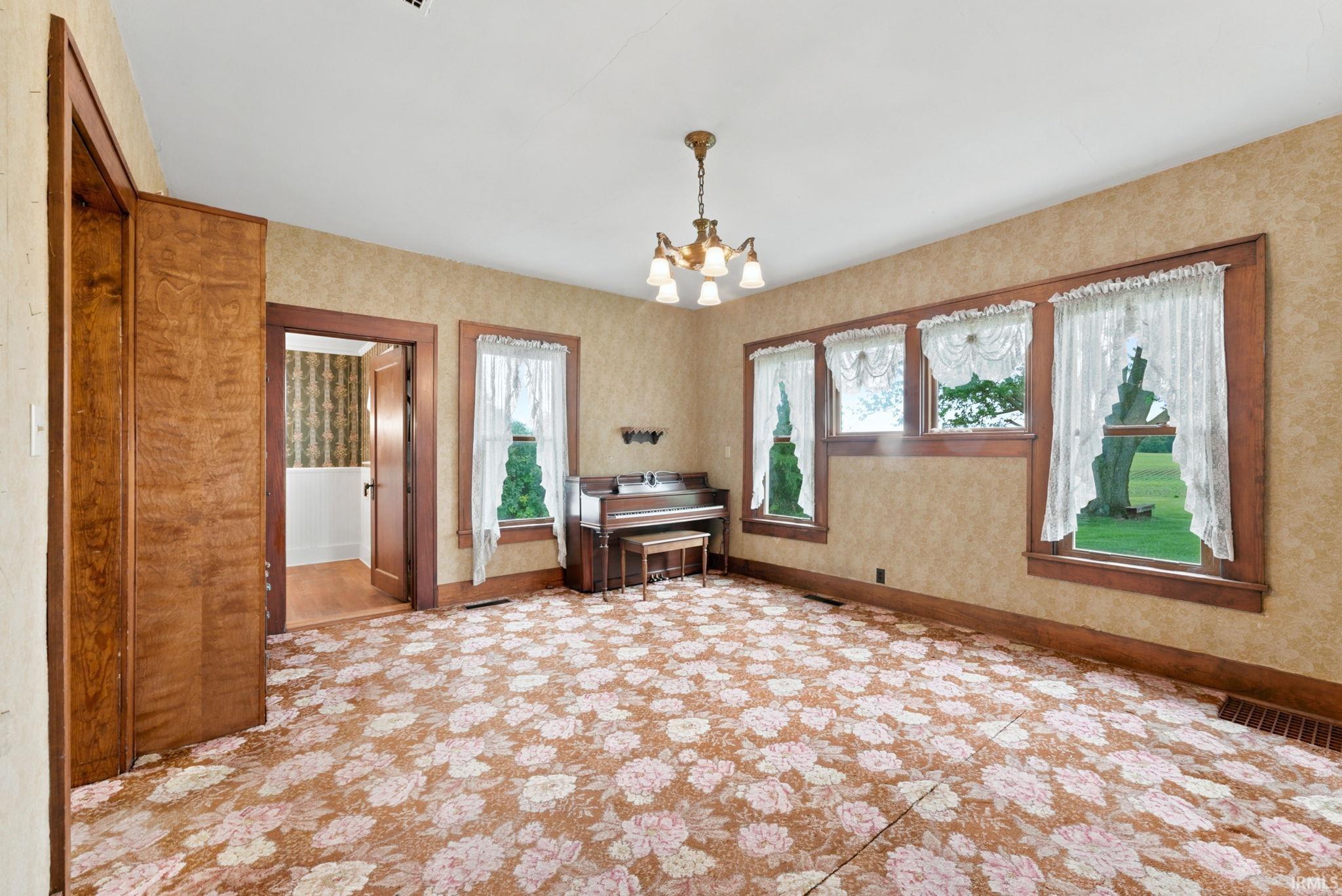 Spacious room with patterned carpeting, featuring wood-trim windows, a brass chandelier, and a wood-paneled doorway